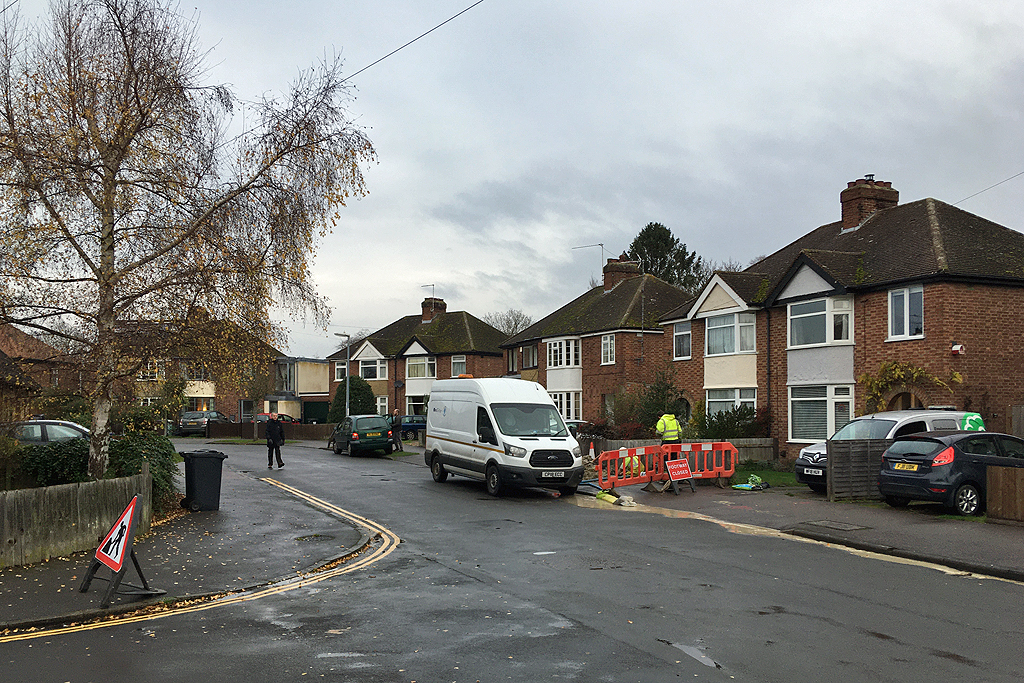 Workers in high-visibility clothing near a white van and road barriers on a residential street.
