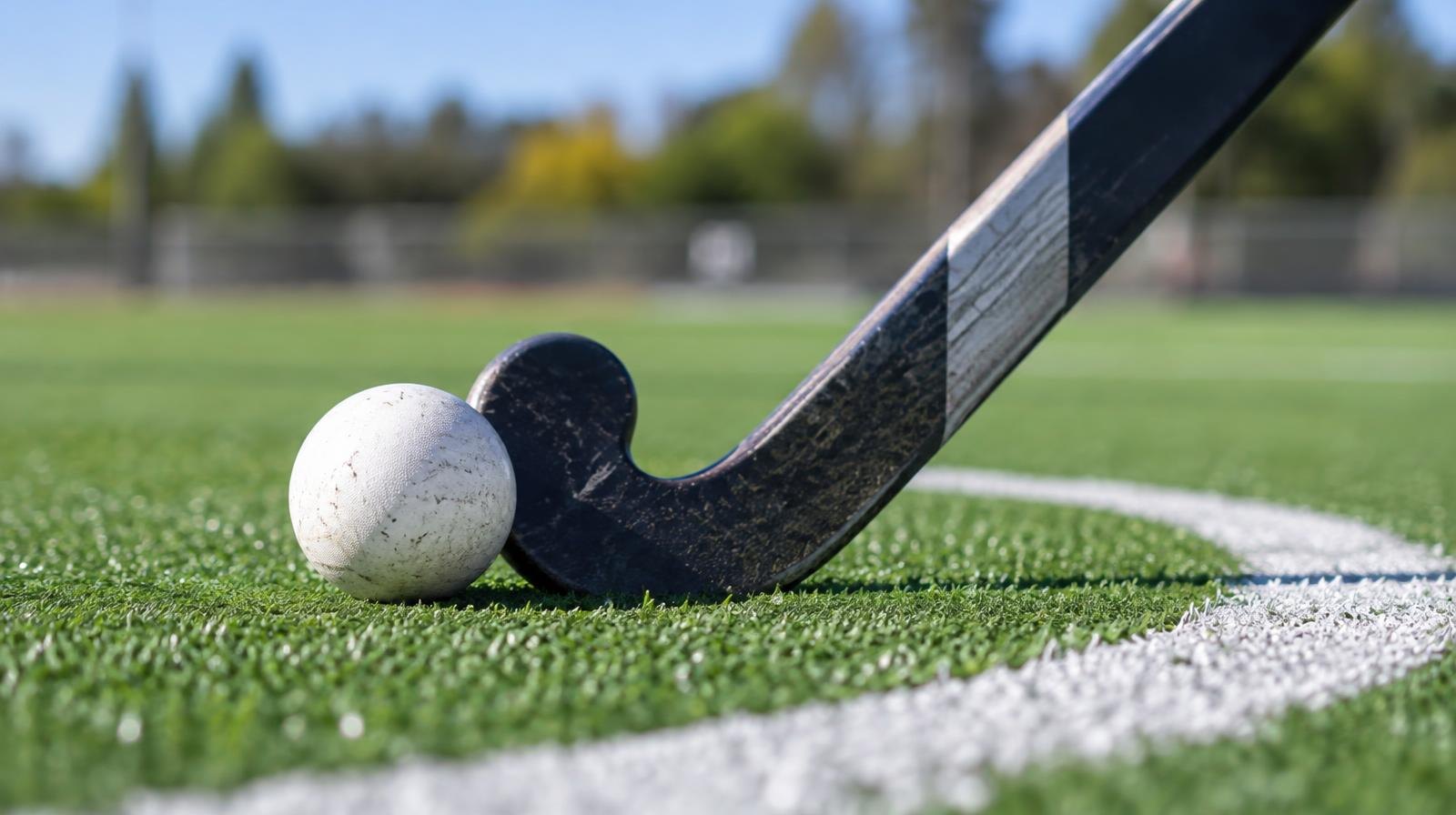 A field hockey stick and ball resting on bright green artificial turf.