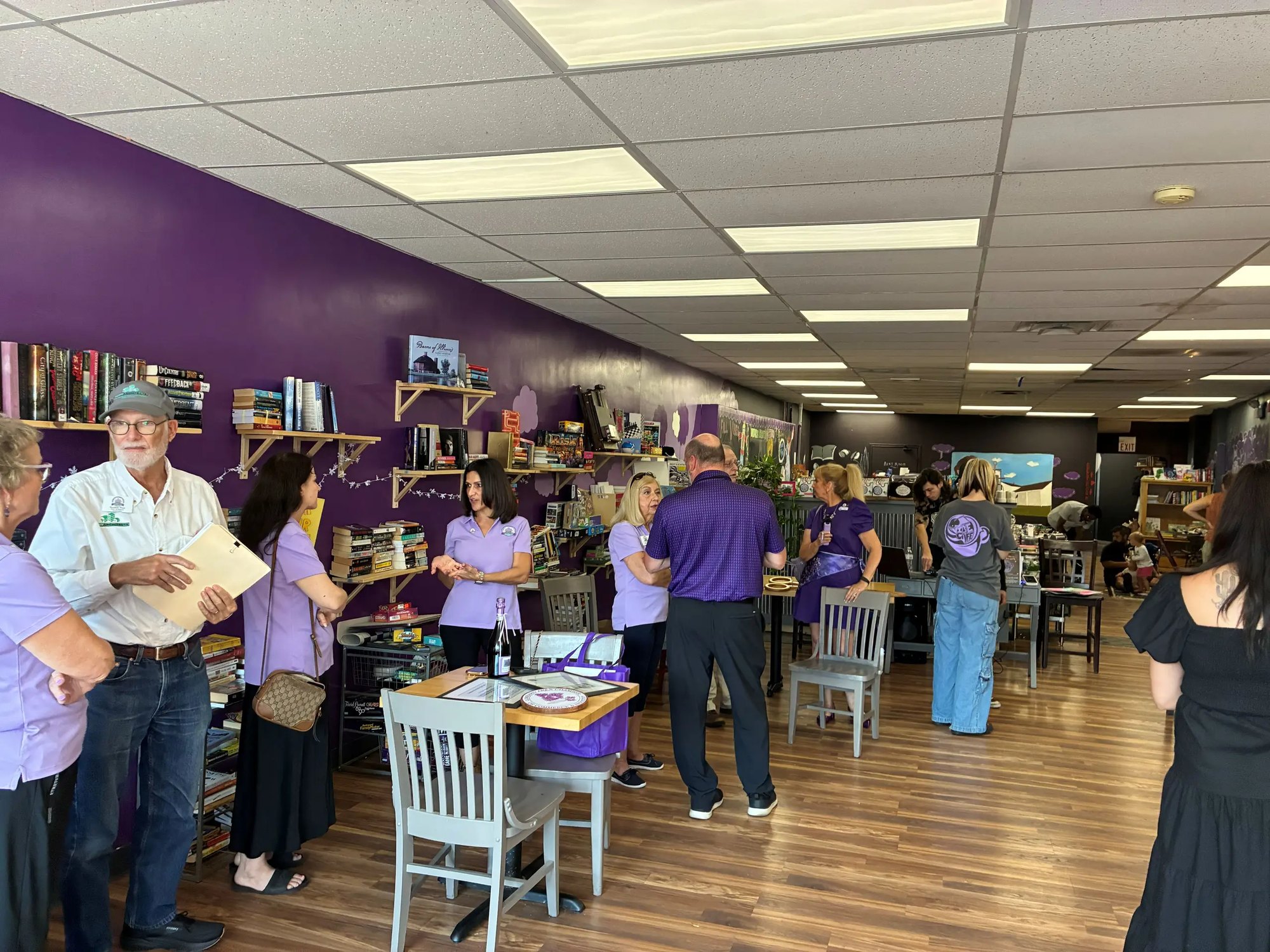 People mingling inside a purple-walled cafe and bookstore during an opening event.