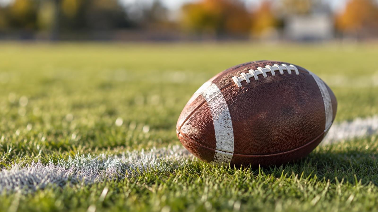 An American football resting on green grass near a white yard line.