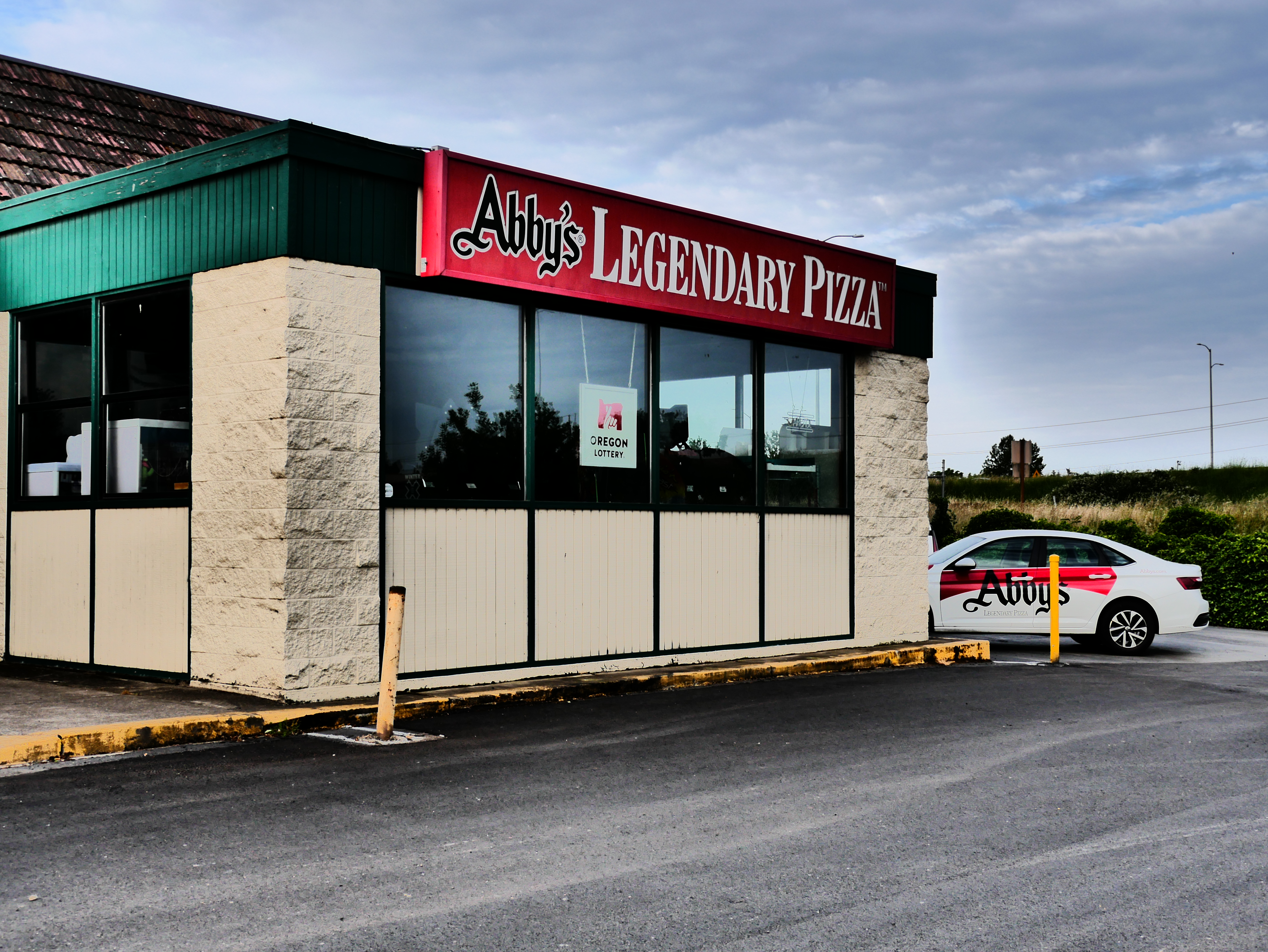 Exterior of a pizza restaurant with red signage and a branded white delivery car.