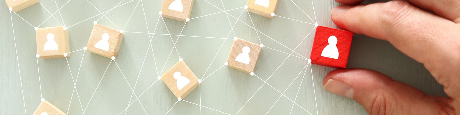 A hand places a red wooden block among connected natural-wood blocks with person icons.