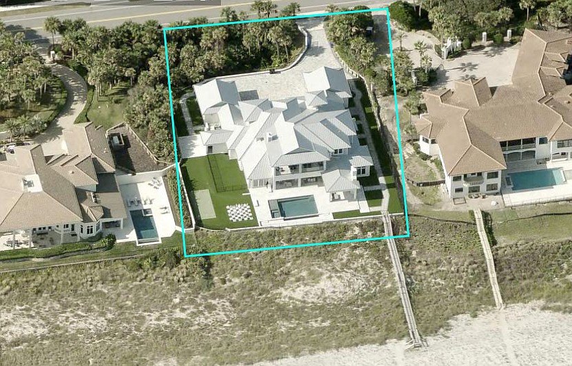 Aerial view of a large white two-story oceanfront home with pool and putting green.