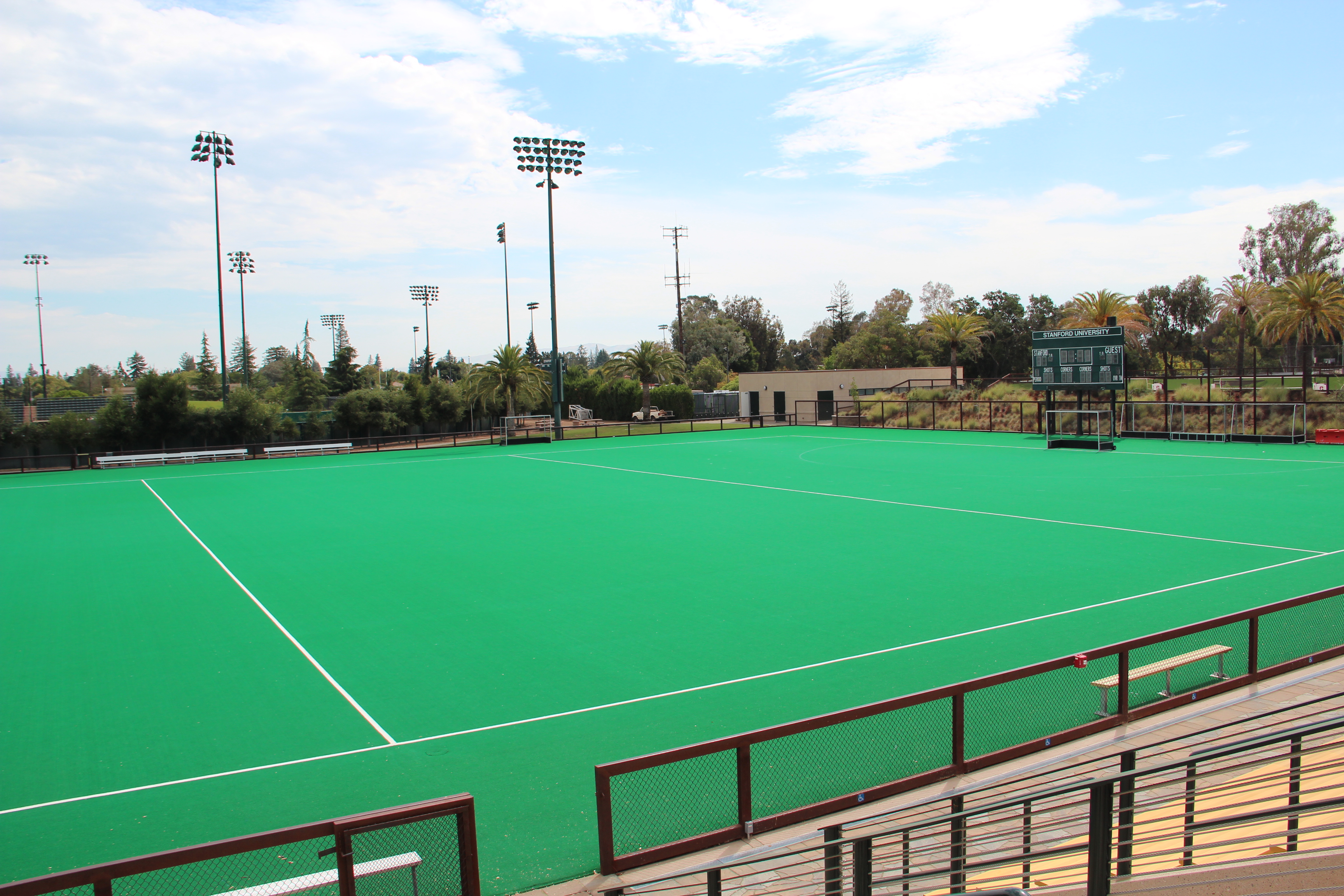 Empty green artificial turf field hockey pitch with stadium lights and bleachers.