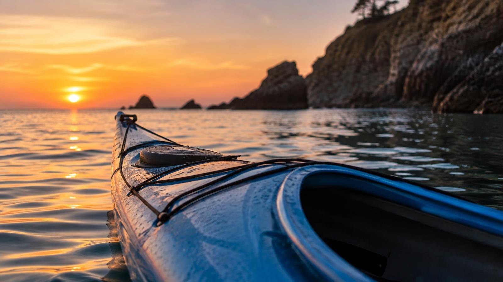 A blue kayak floating on calm ocean water near a rocky cliff at dusk.