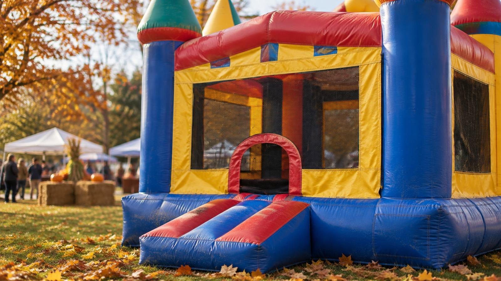 A colorful inflatable bounce house castle on green grass with autumn leaves nearby.
