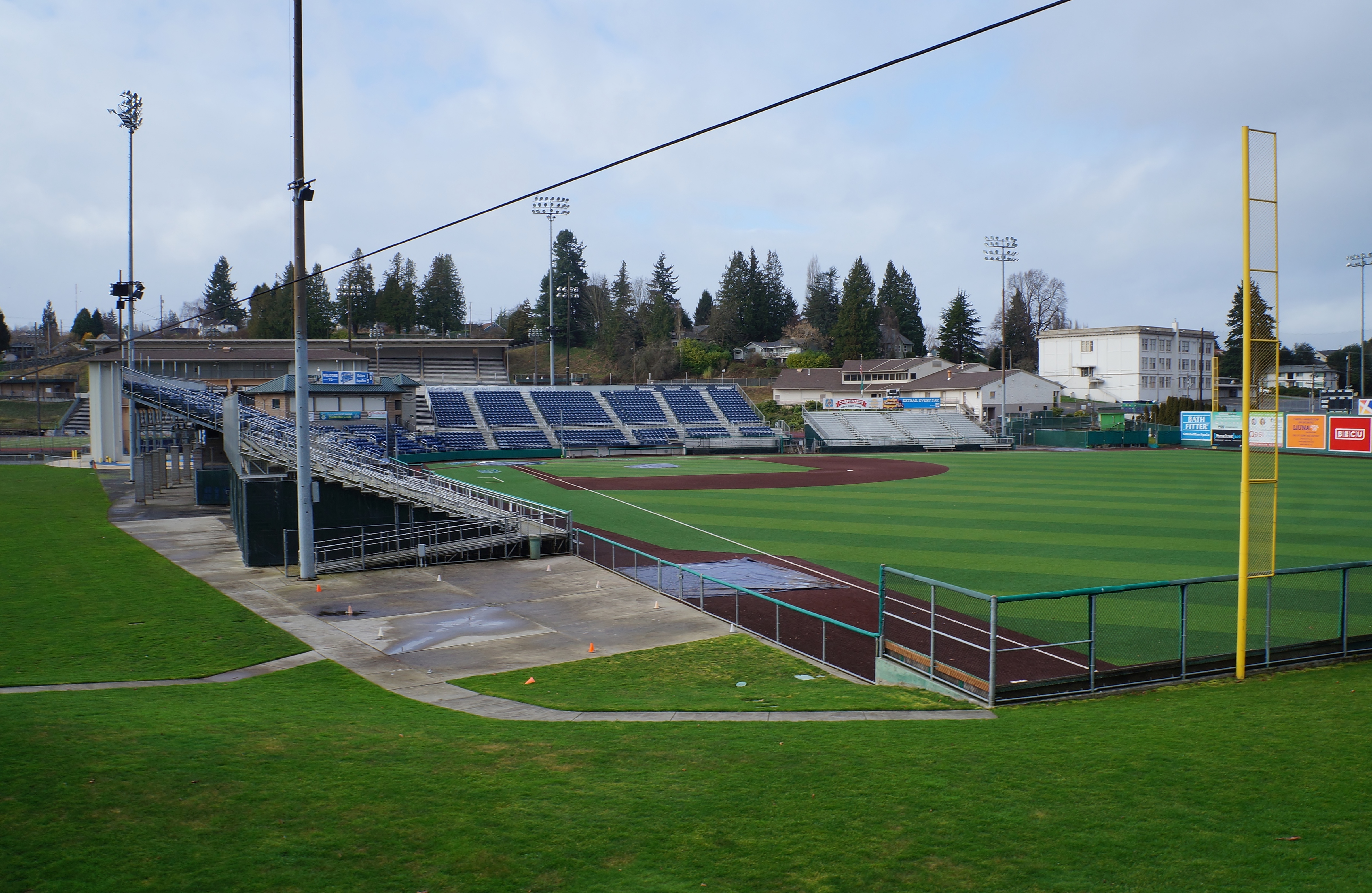 Blue bleacher seating and baseball diamond at a minor league ballpark on an overcast day.