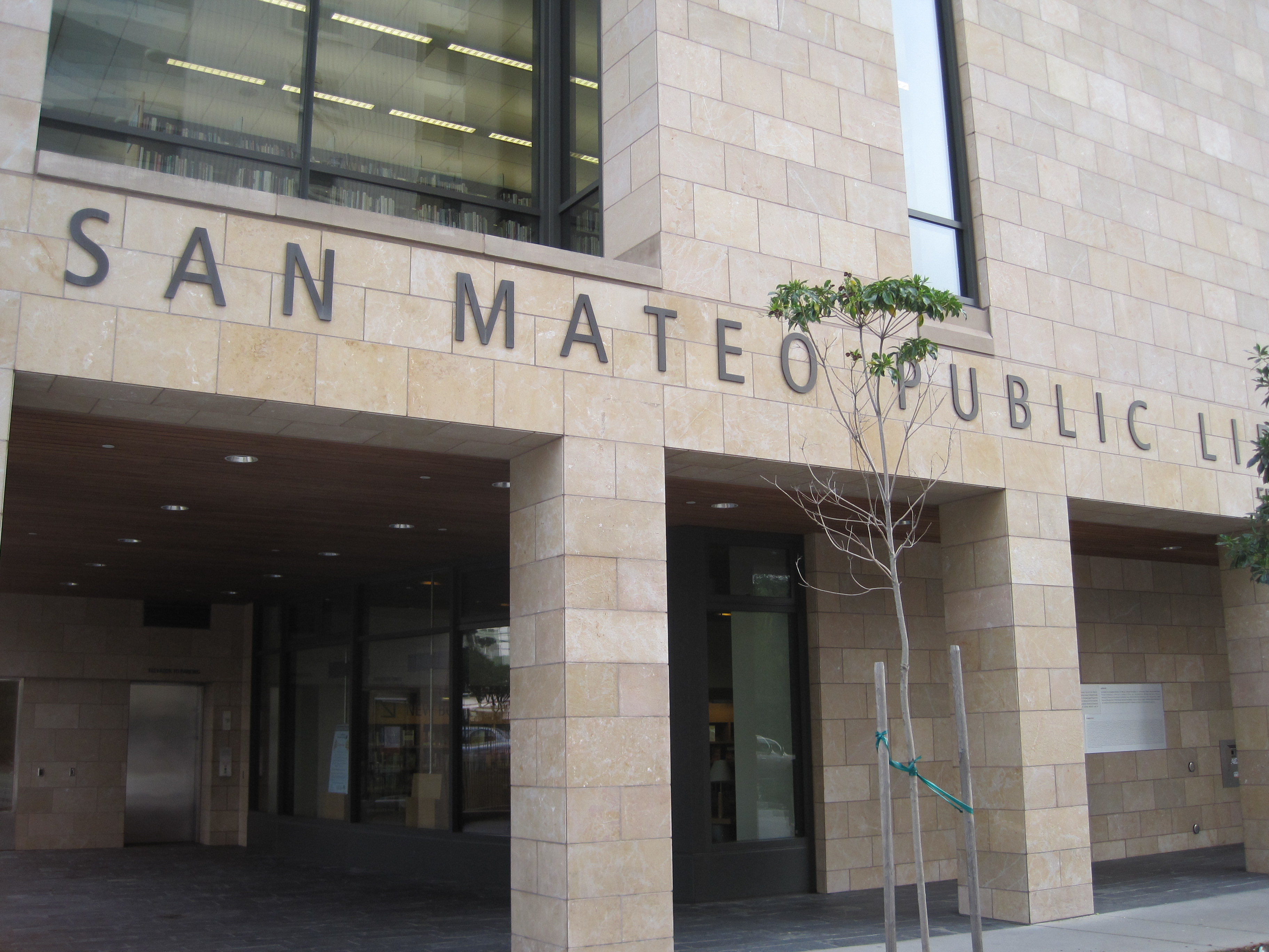 Front entrance of a public library with stone columns, partial signage, and a covered canopy.