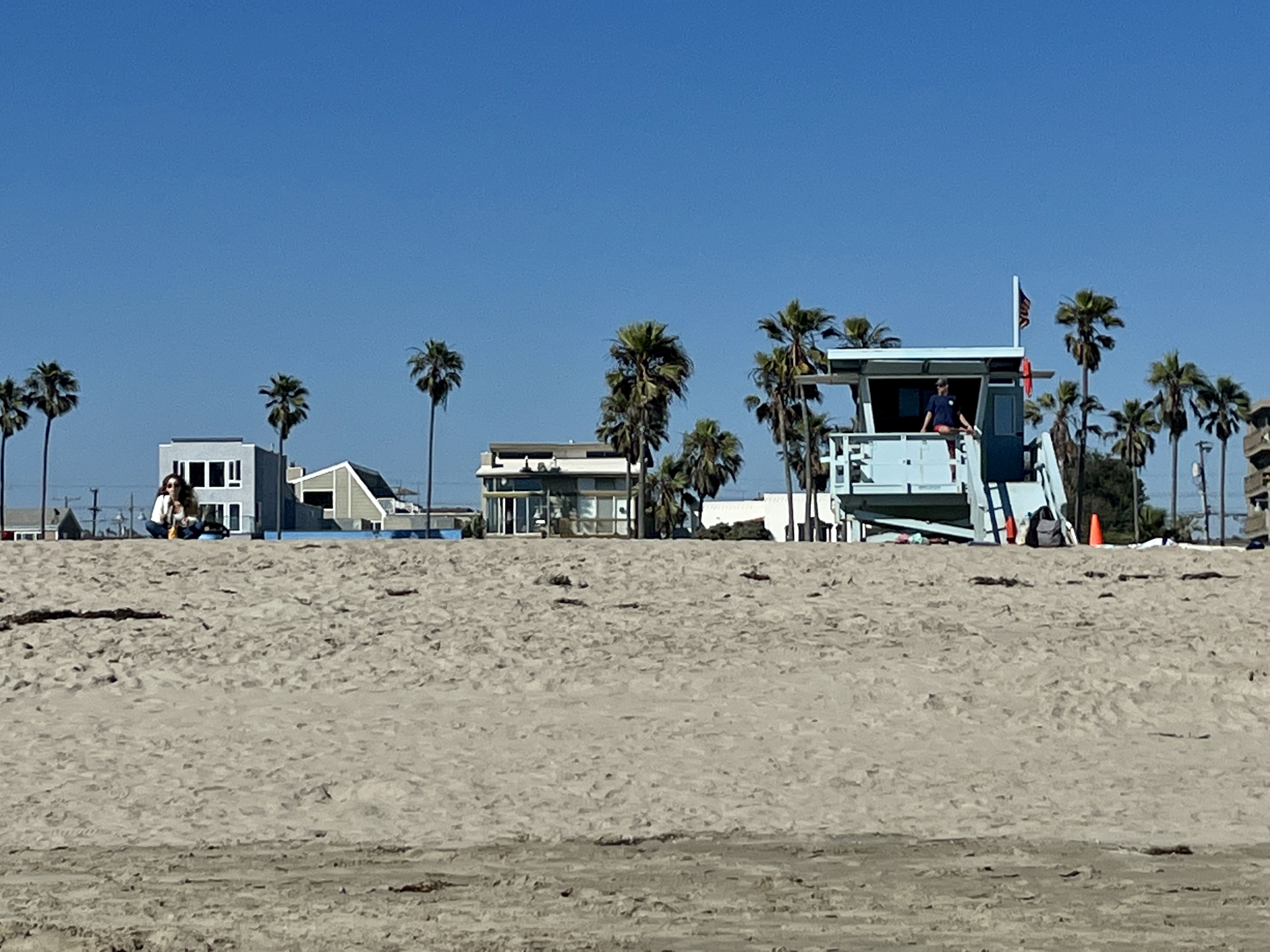 Elevated lifeguard tower on a sunny sandy beach with palm trees behind it.