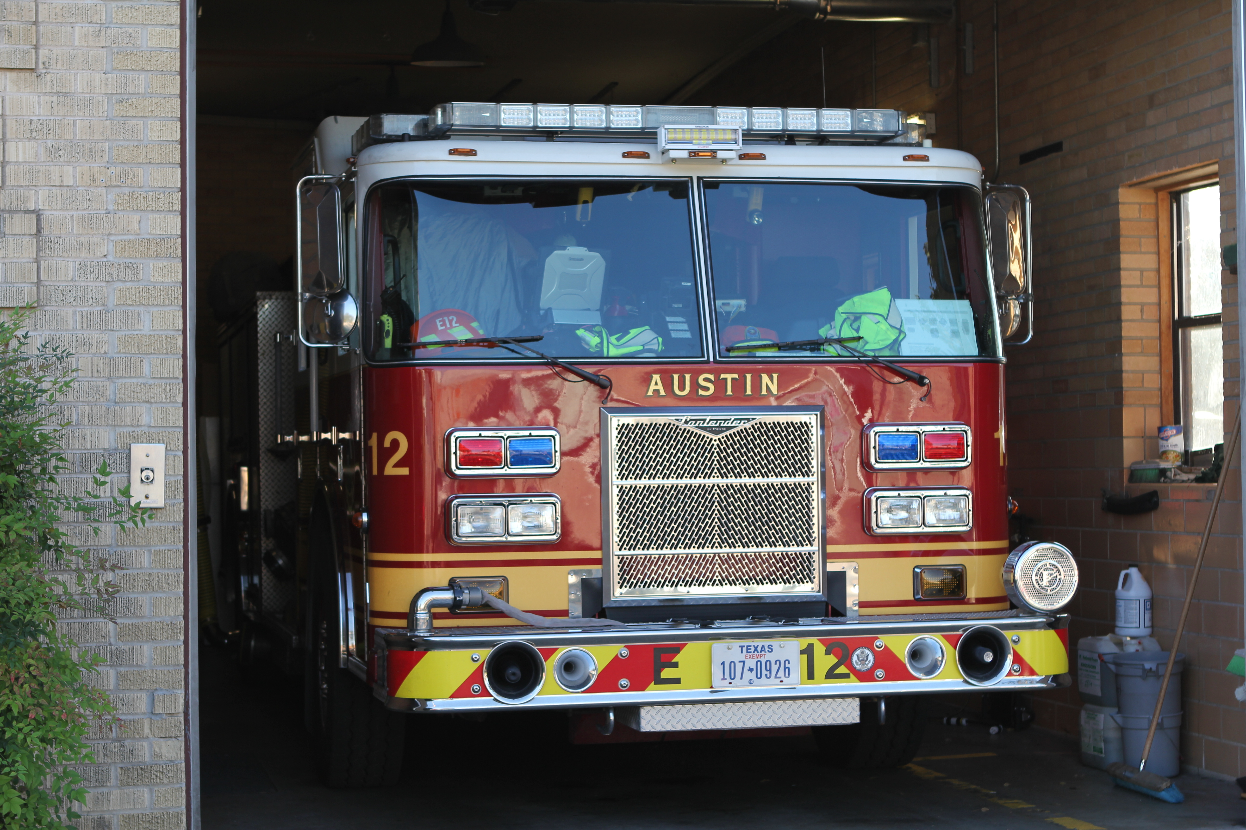 Red fire engine parked inside a fire station bay, viewed from the front.