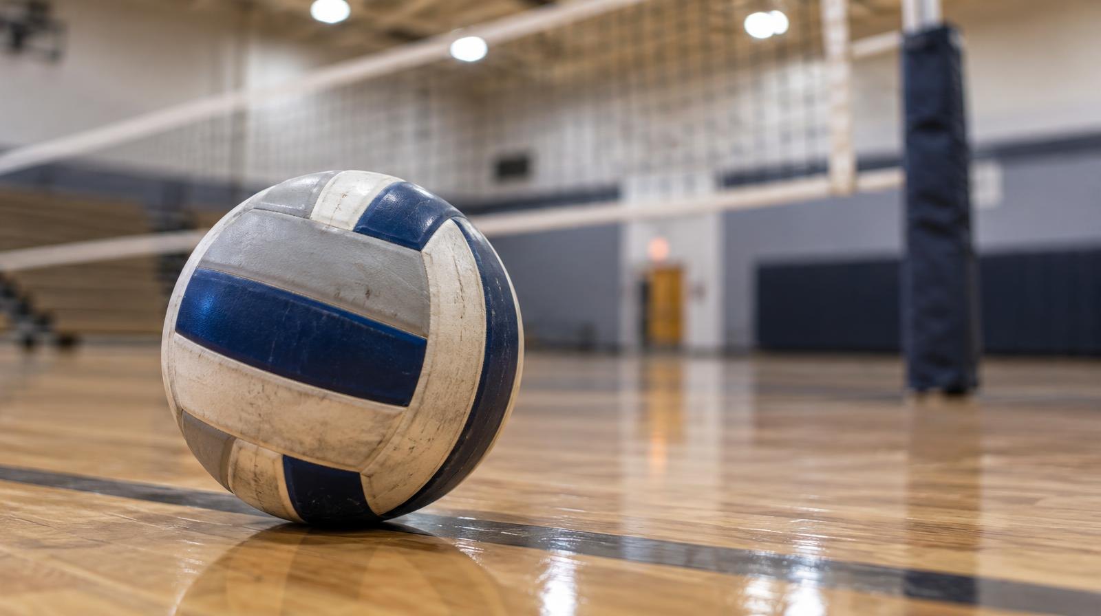 A volleyball resting on a hardwood gym floor near the net.