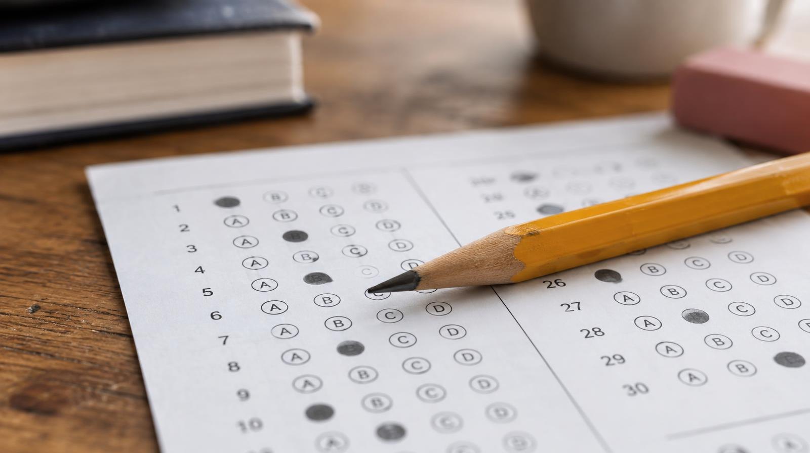 A sharpened pencil resting on a multiple-choice answer sheet on a wooden desk.