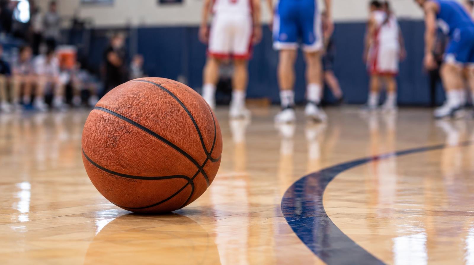 A basketball resting on a polished hardwood gymnasium floor.