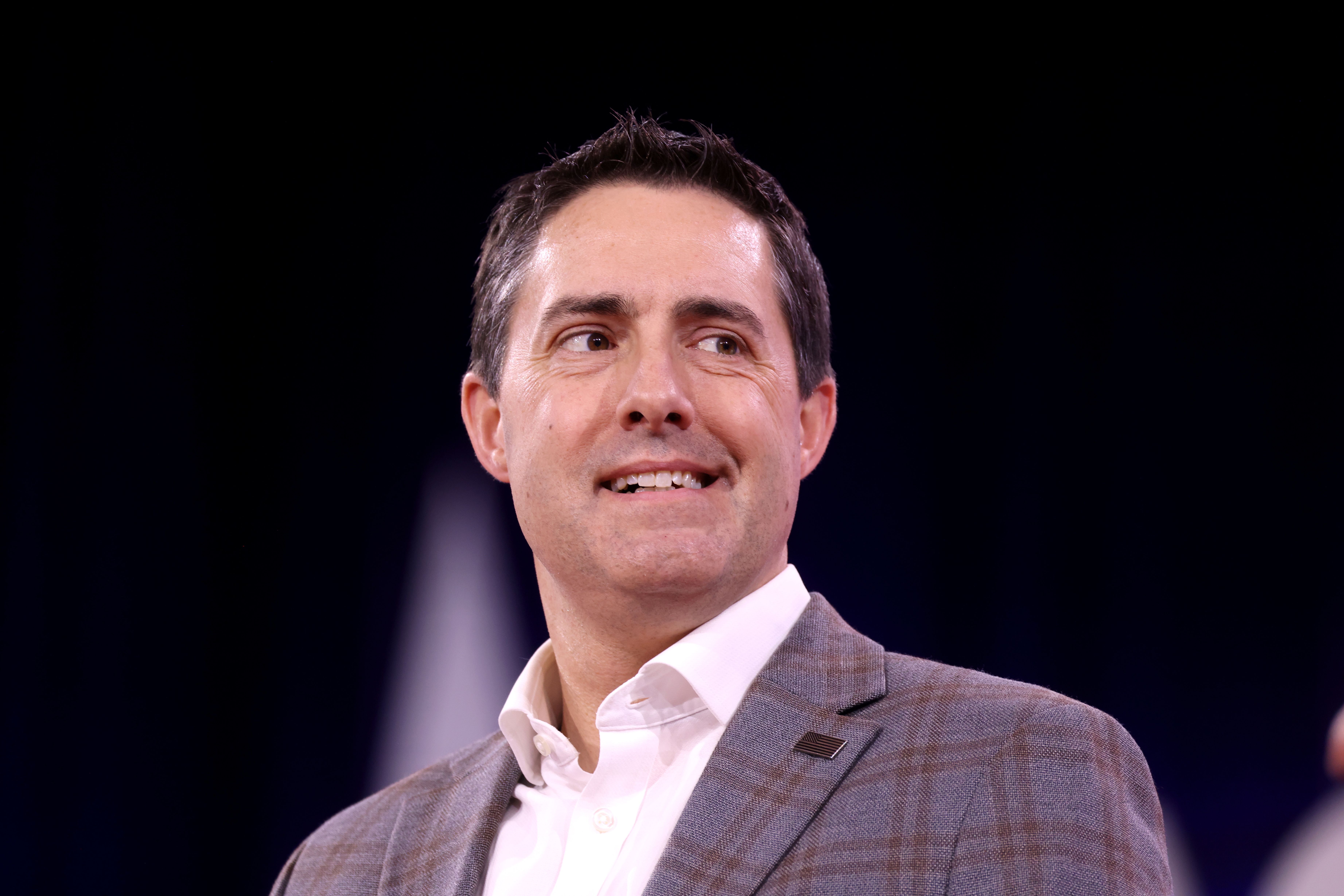 Man in grey blazer smiling and looking upward at a speaking event.