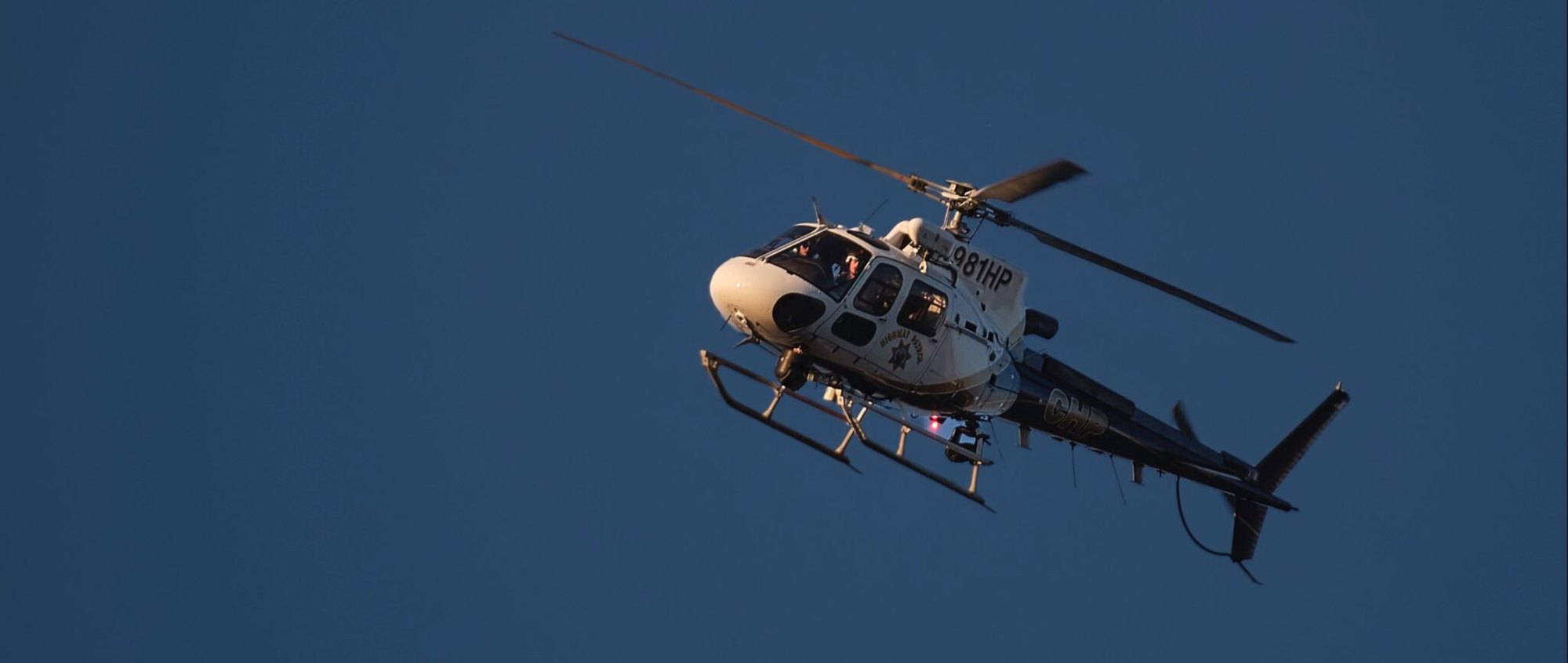 A CHP helicopter in flight against a dark blue sky with agency markings visible on the tail.