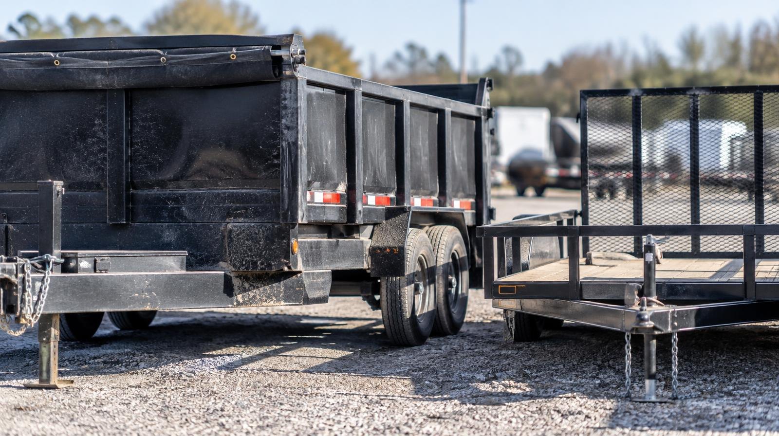 A dump trailer and utility trailer parked side by side on a gravel yard.