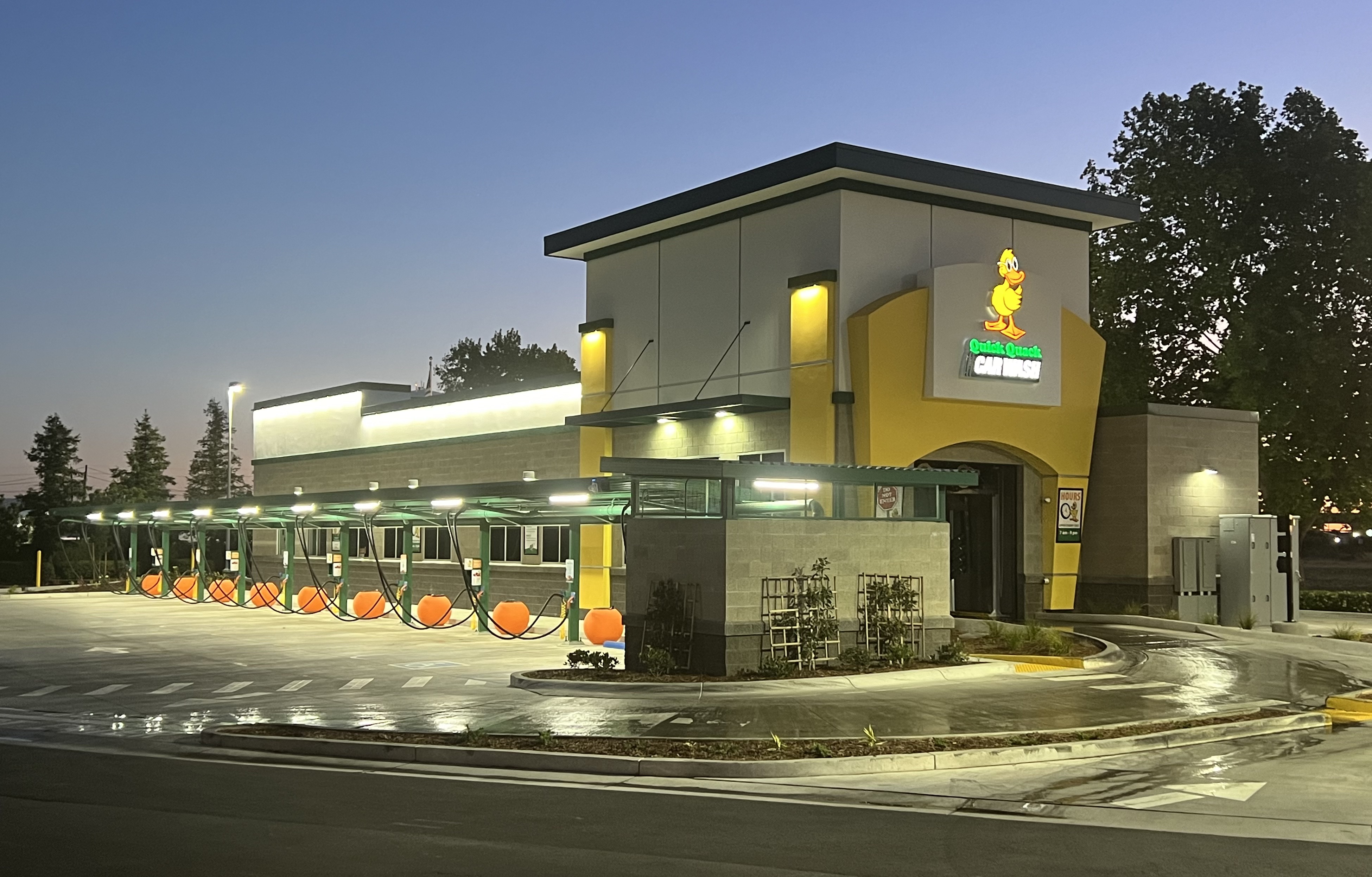 Quick Quack Car Wash building exterior at dusk, yellow facade with illuminated wash bays.