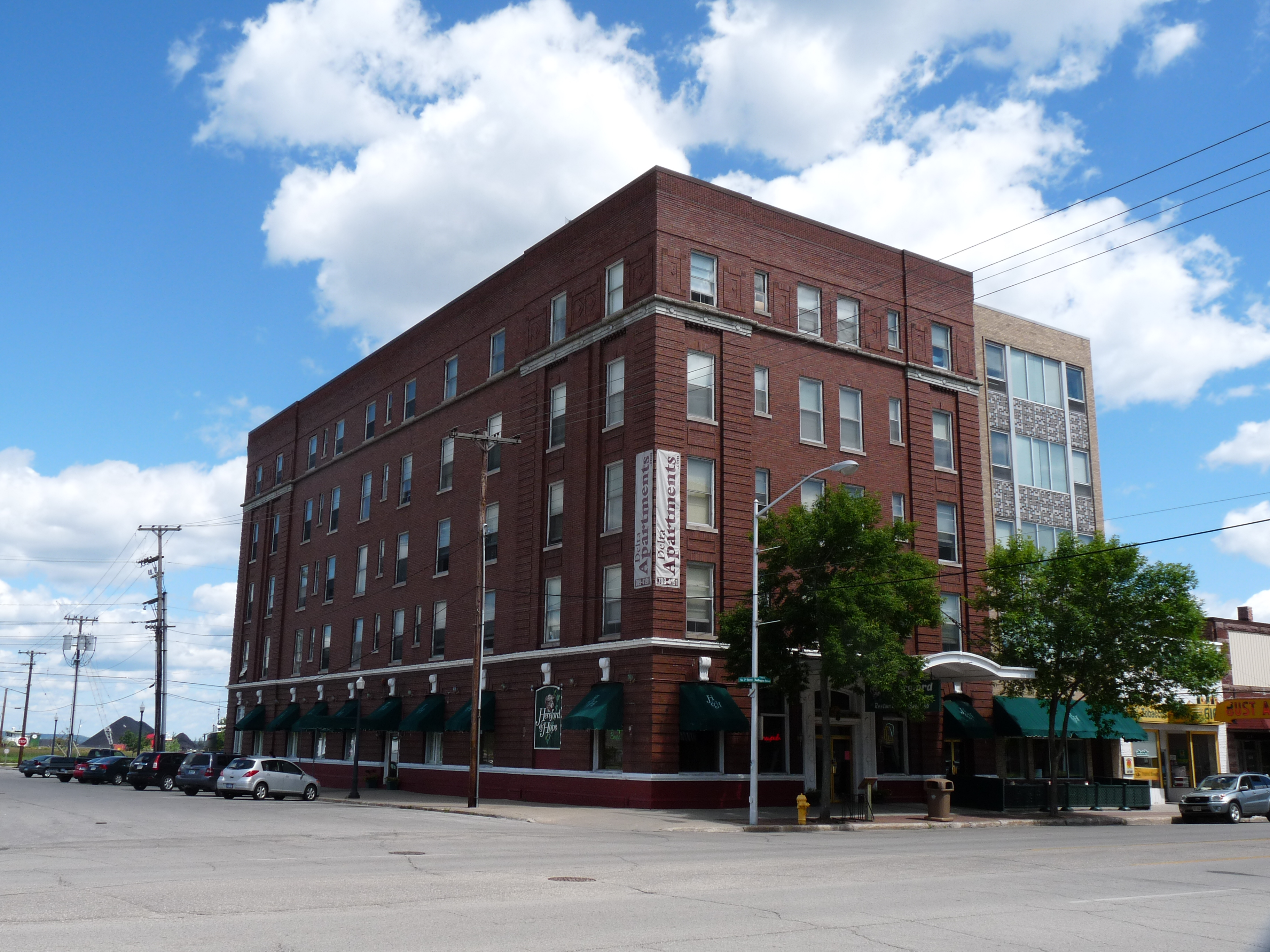 Five-story red brick corner building with green awnings on a downtown street.