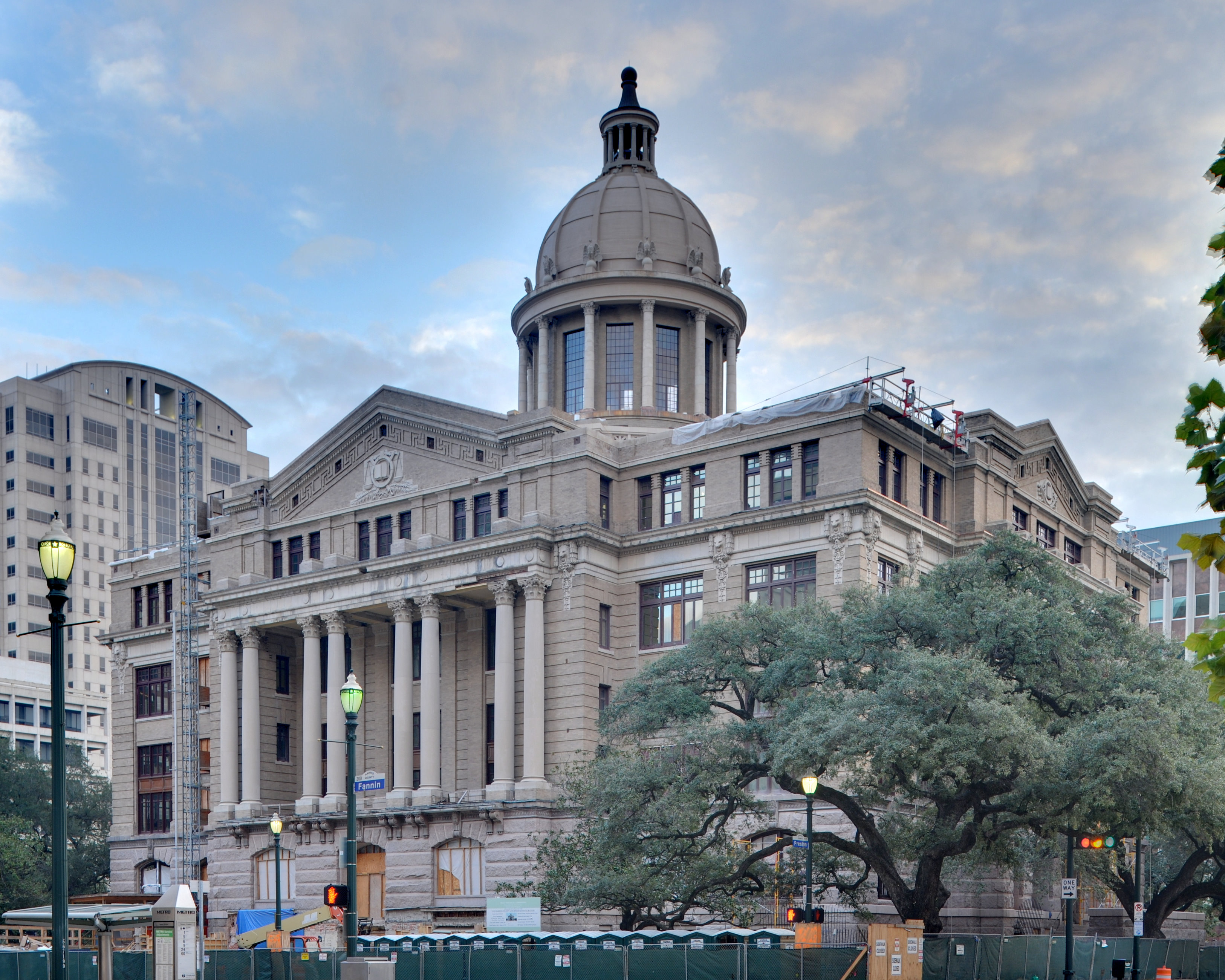Neoclassical domed courthouse building with columns, surrounded by trees and tall buildings.
