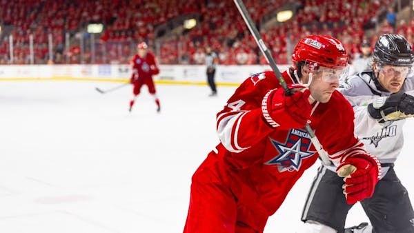 Hockey player in a red jersey battles an opponent along the boards in a packed arena.