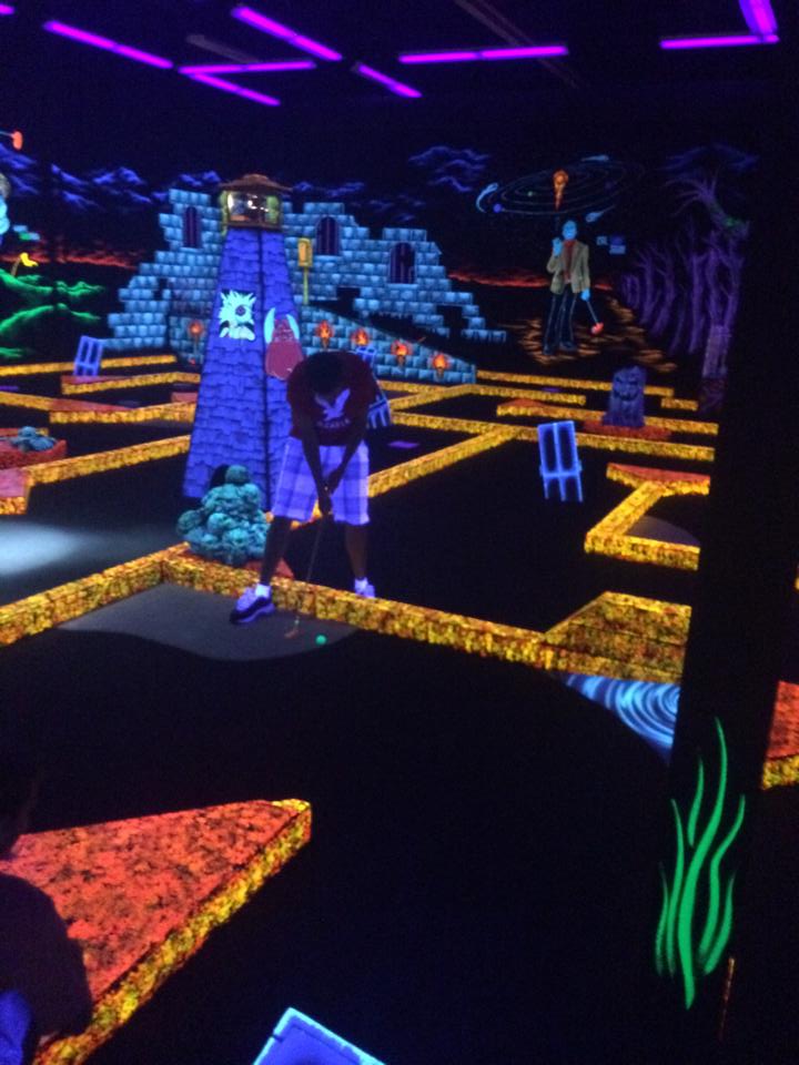 Person putting on a neon-lit indoor glow-in-the-dark mini golf course.