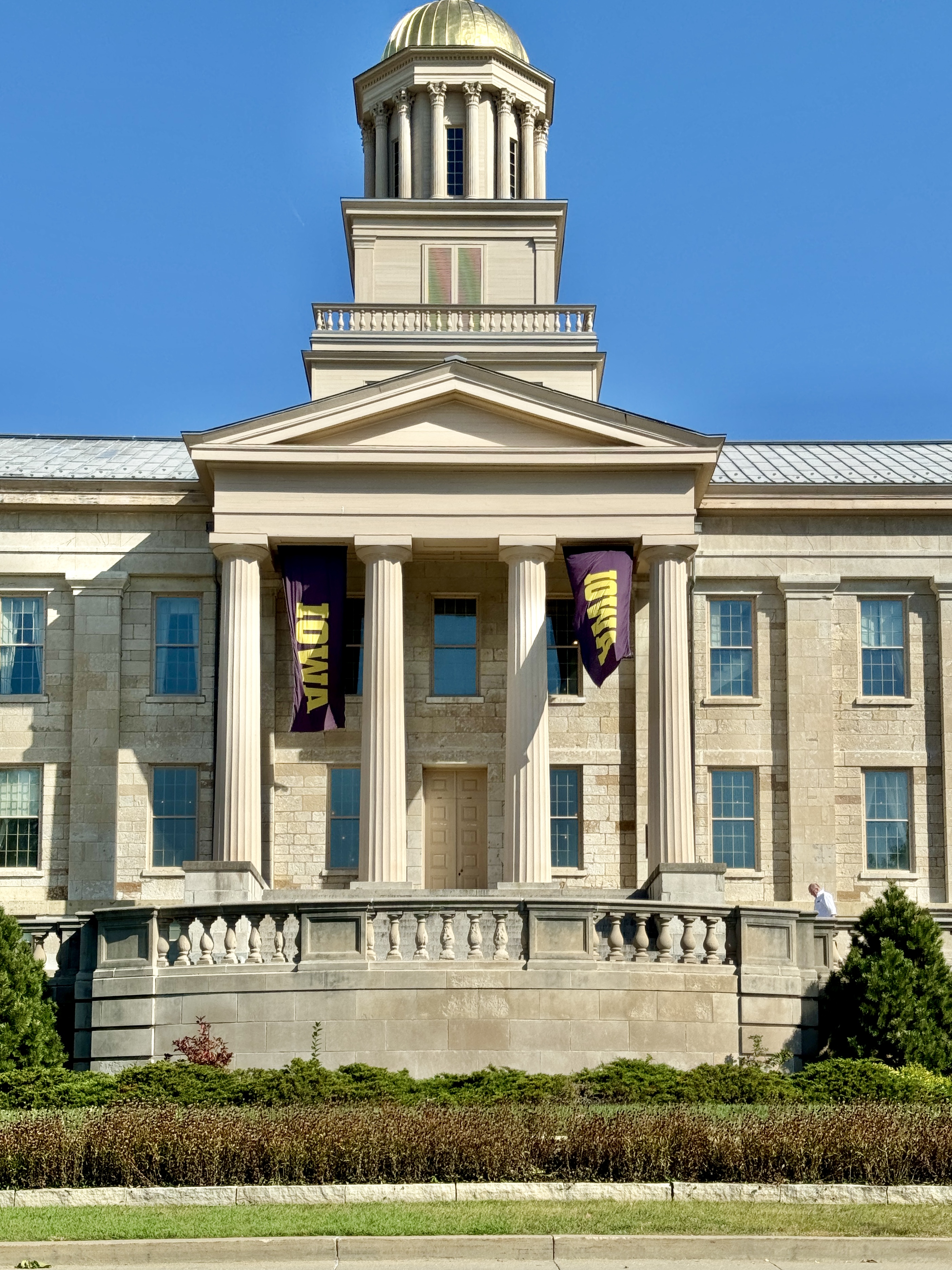 Greek Revival limestone building with a gold-domed cupola and purple university banners on its columns.