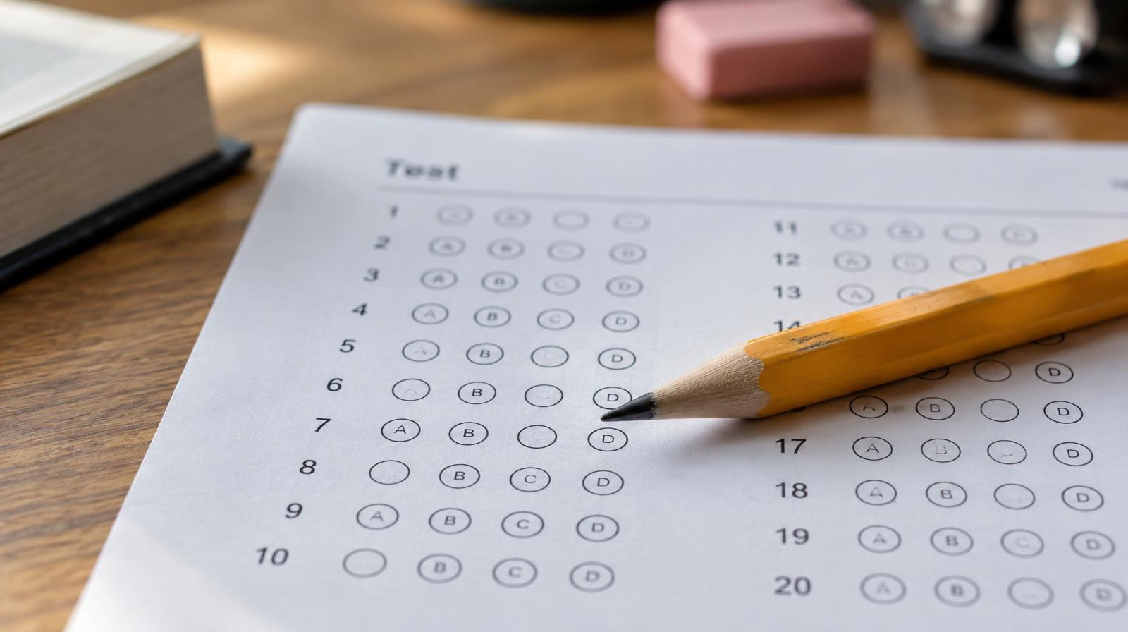 A sharpened pencil resting on a blank multiple-choice answer sheet on a wooden desk.