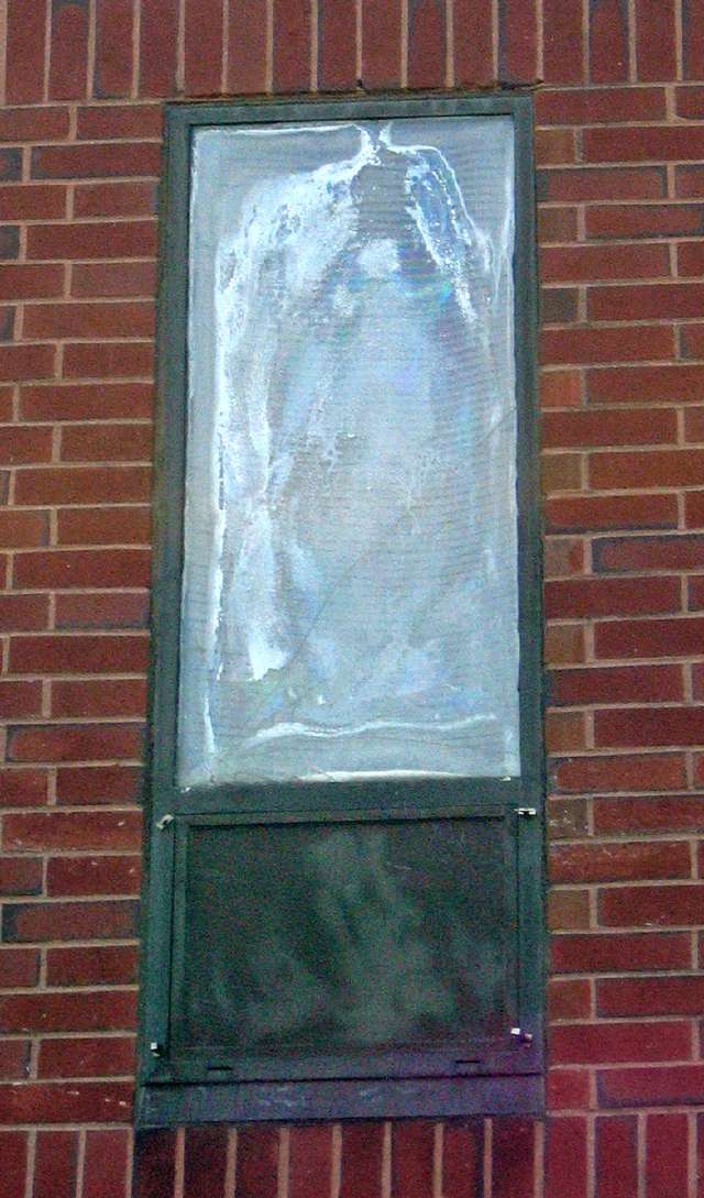 Frosted glass window in a green metal frame on a red brick hospital exterior wall.