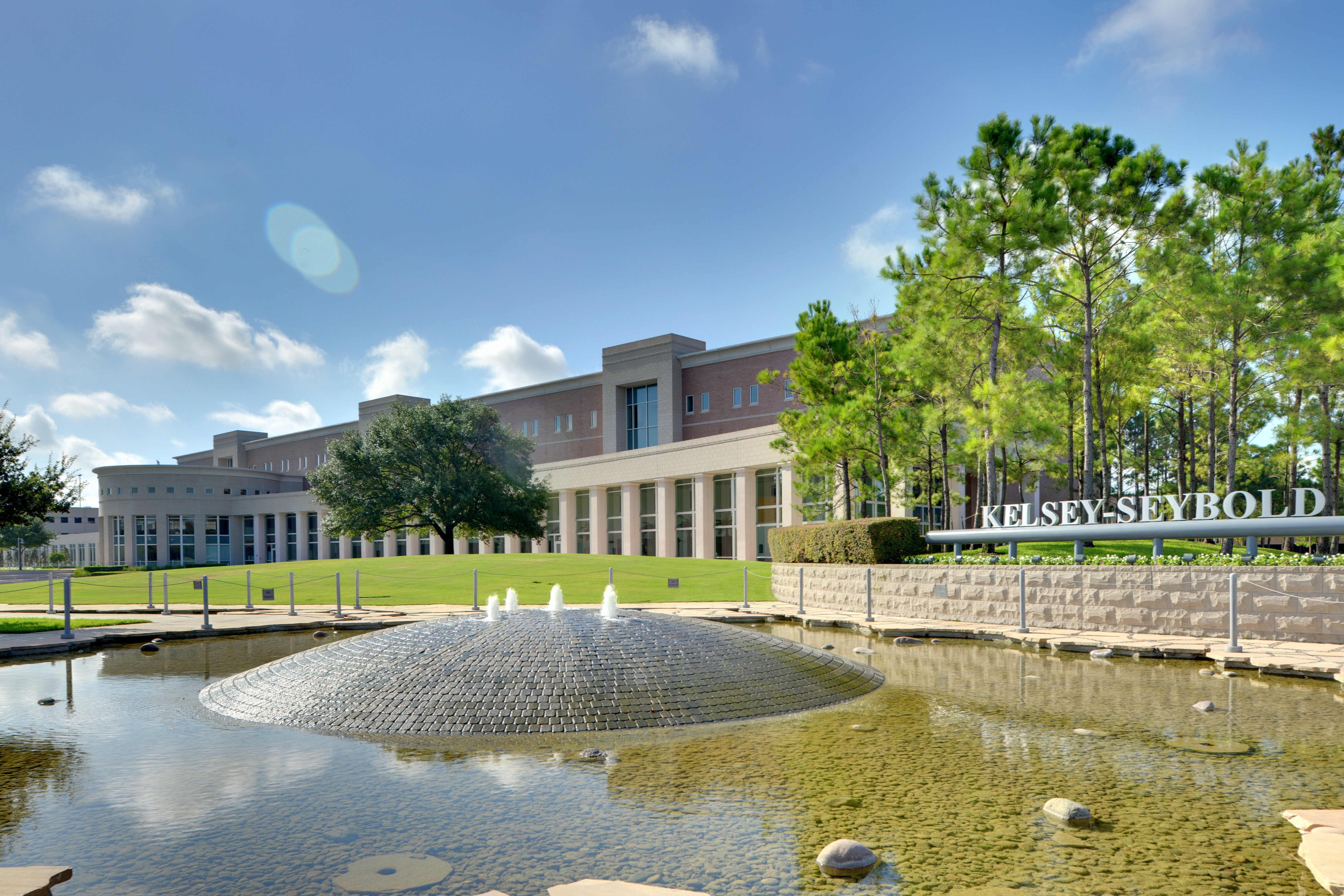 Exterior of a multi-story brick clinic building with a fountain pond and manicured lawn in front.