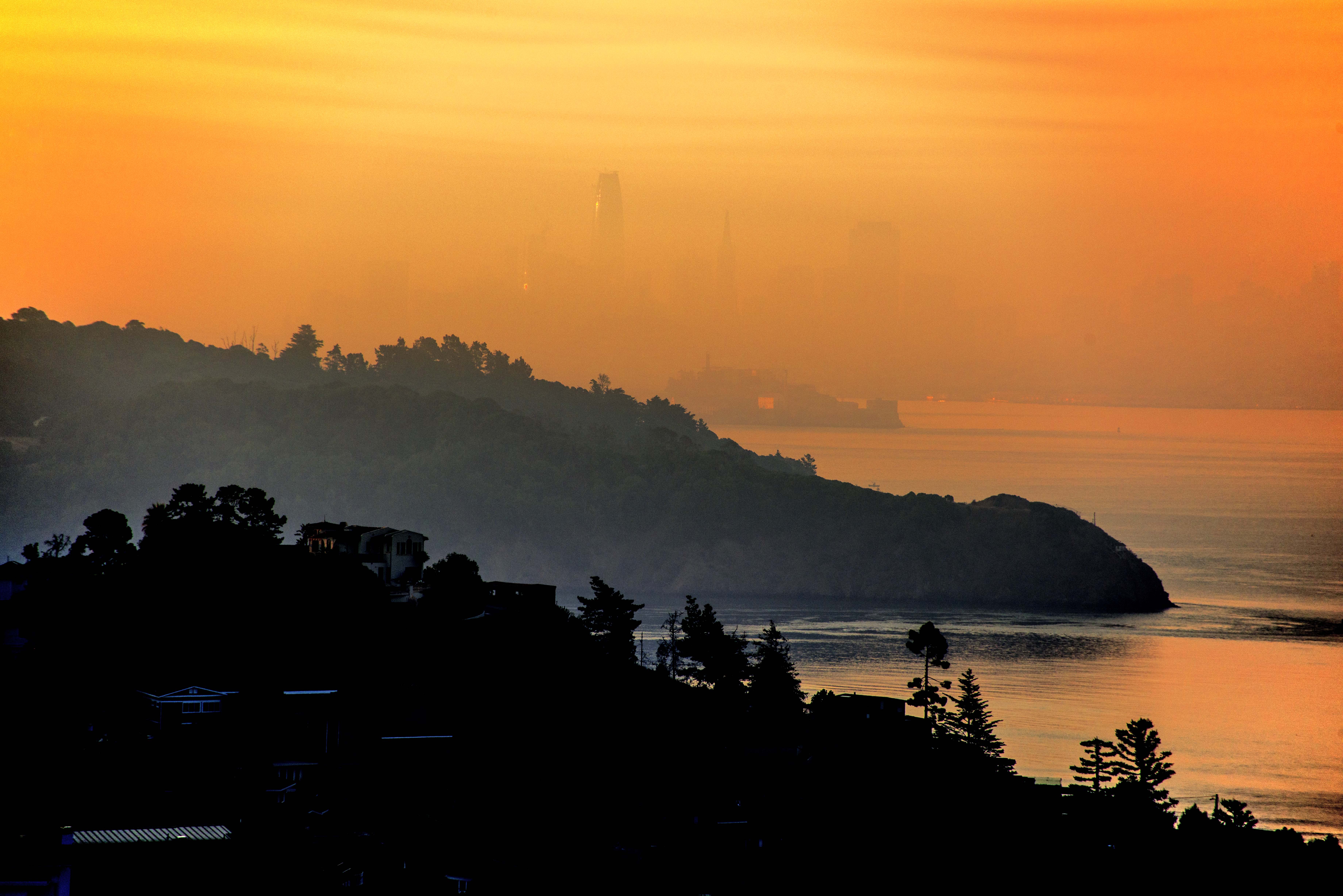 Orange smoke-filled sky over the San Francisco Bay at sunrise, with hazy silhouetted hills.