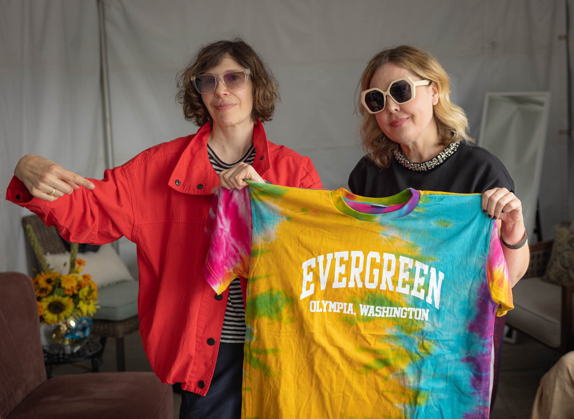Two women hold up a colorful tie-dye shirt reading 'Evergreen Olympia, Washington.'
