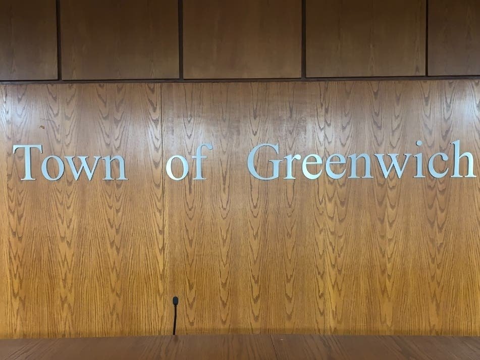 Silver letters spelling 'Town of Greenwich' mounted on a wood-paneled wall.