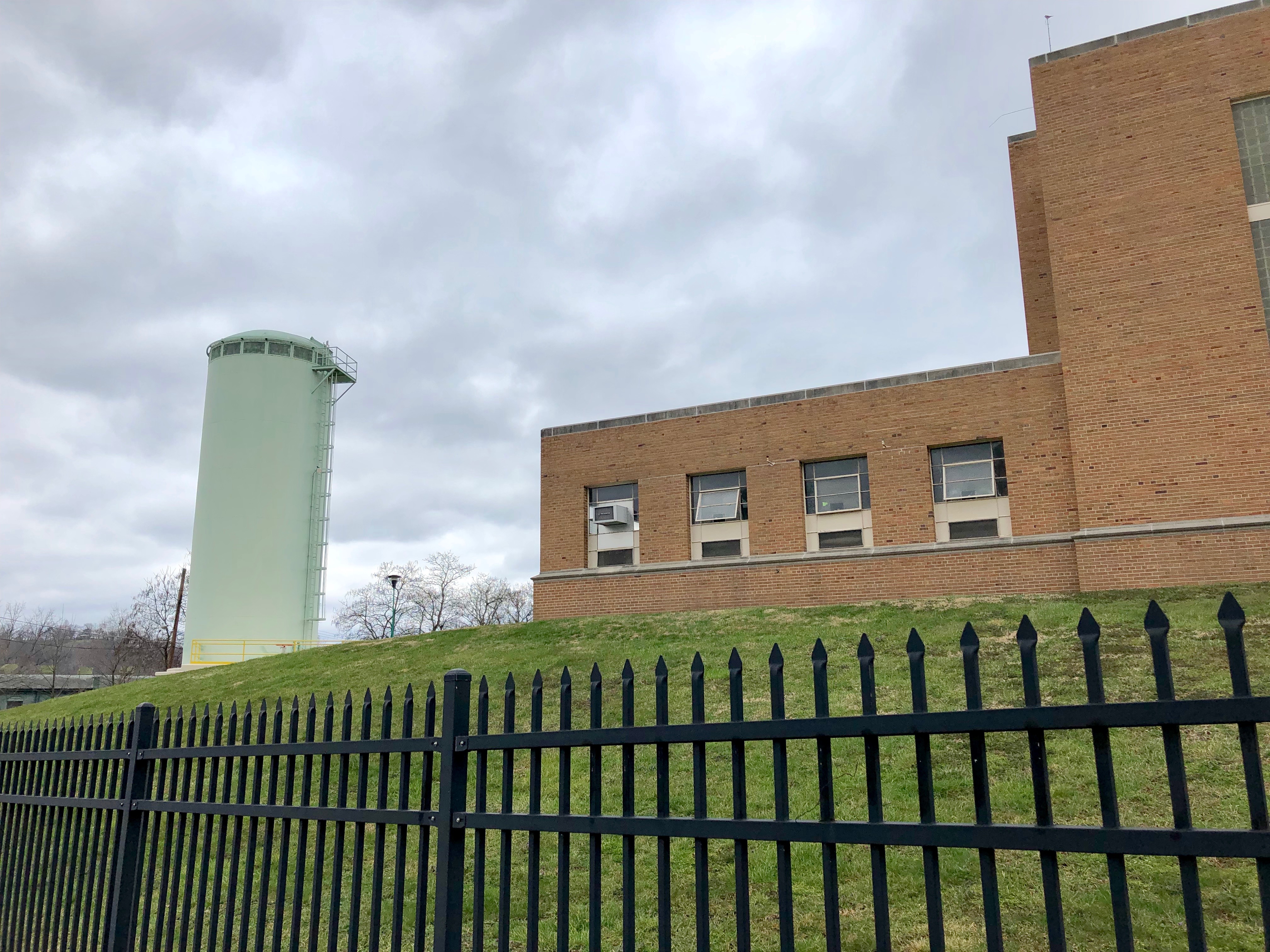 Brick water utility building with a green water tower behind an iron fence.