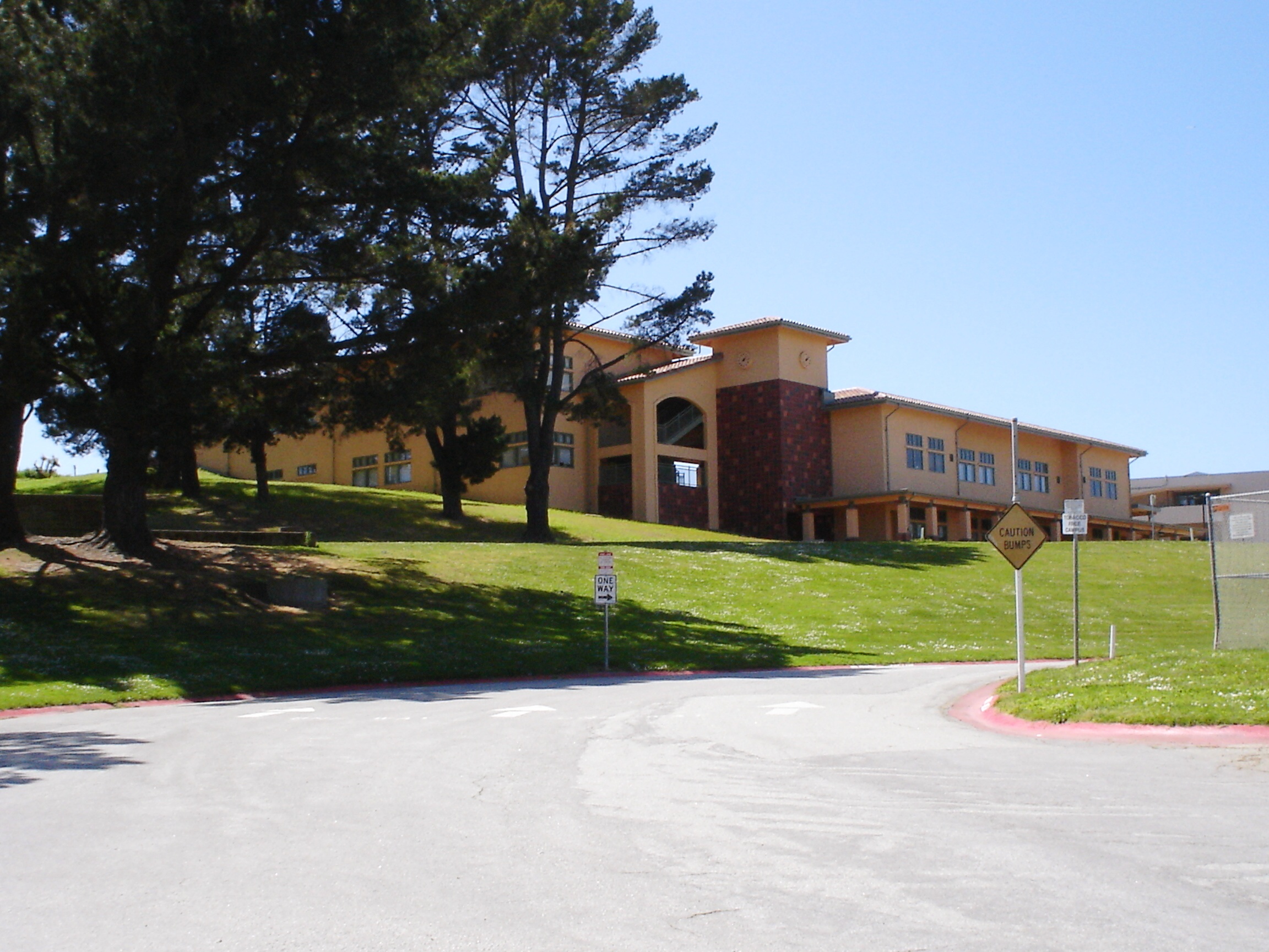 Two-story yellow stucco school building with arched entrance set on a grassy hillside.