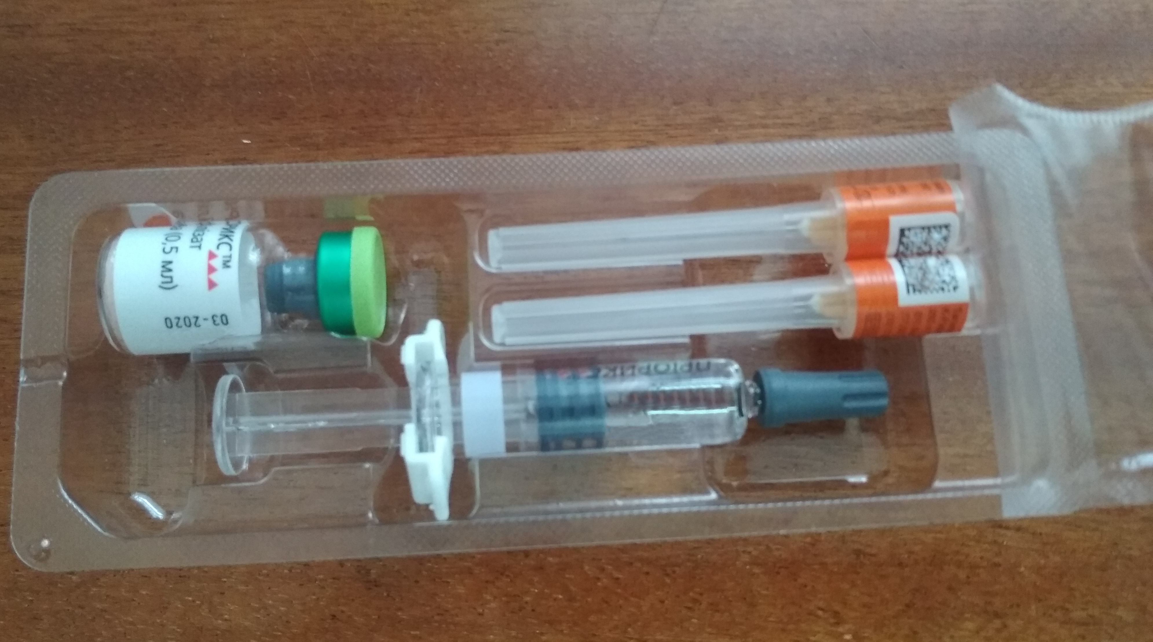 MMR vaccine kit in a plastic tray showing a vial, two needles, and a pre-filled syringe on a wooden surface.