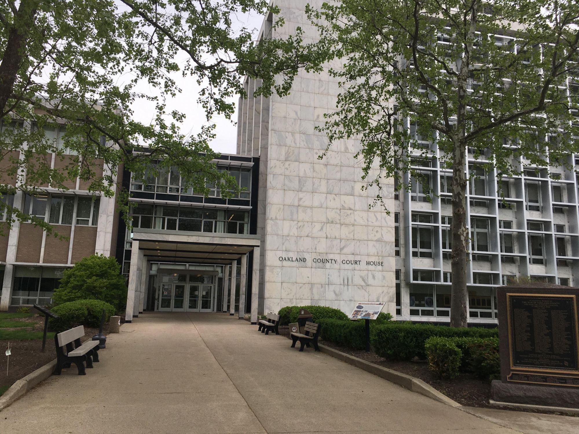 Exterior of the Oakland County Court House, a modernist stone building with glass entrance and trees.