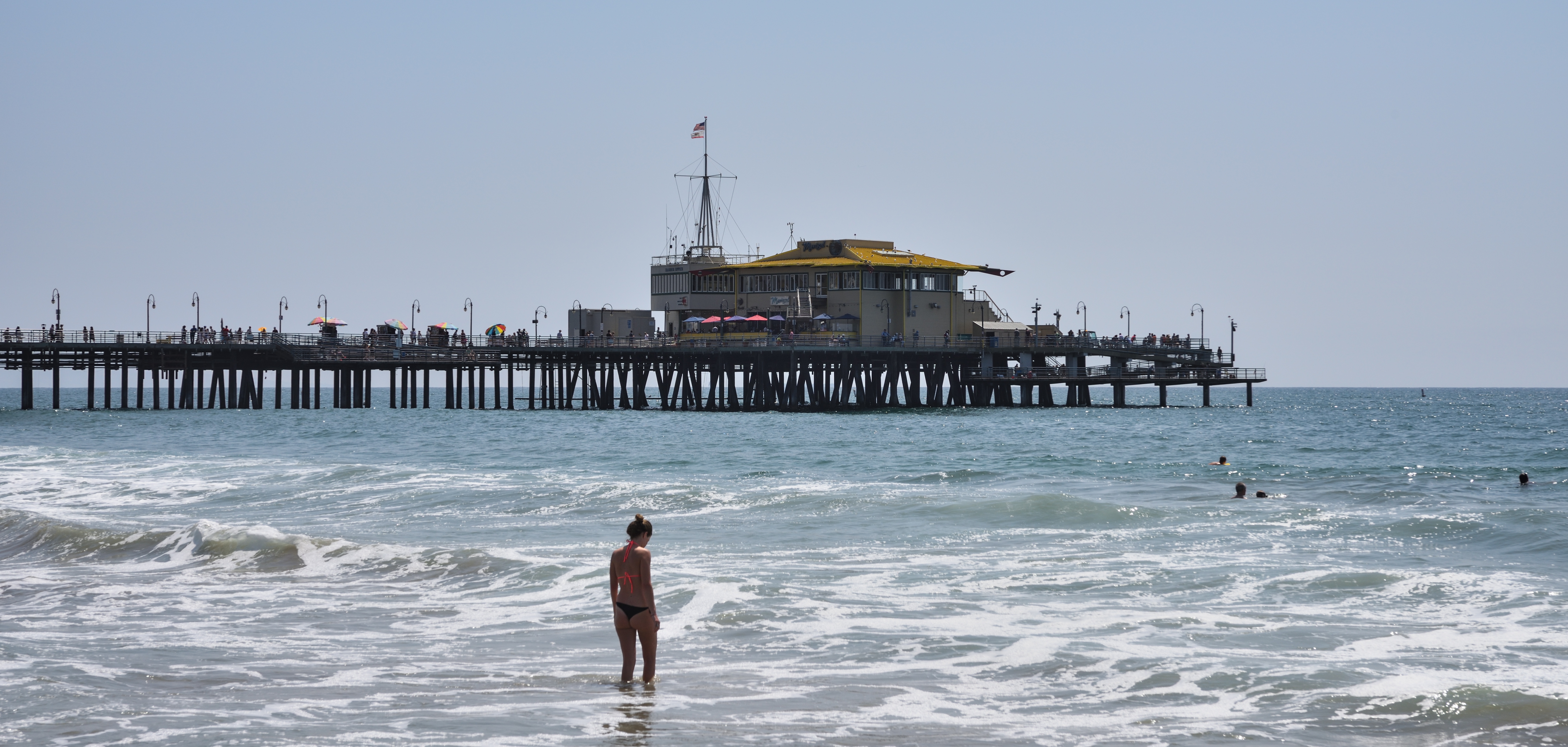 The Santa Monica Pier stretches over the ocean as seen from the sandy beach below.