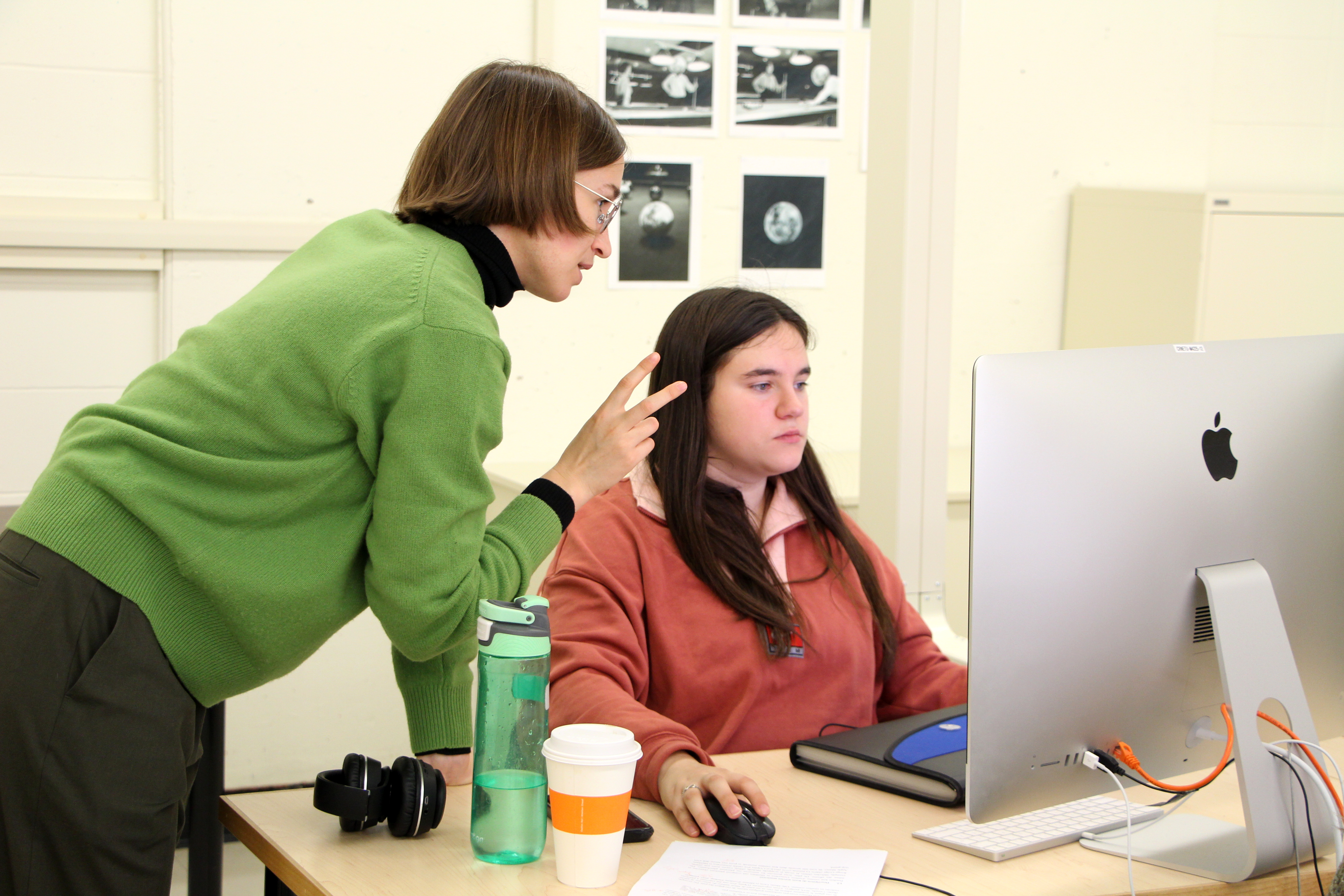 A student seated at a desktop computer receives help from an instructor.