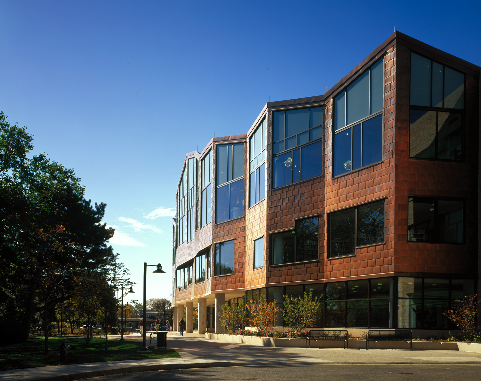 Modern library building with copper facade and open plaza under blue sky.