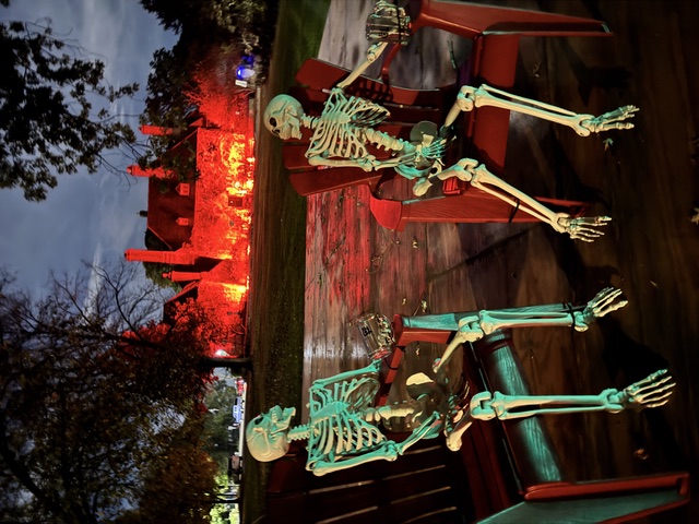 Two fake skeletons sit on chairs outside a glowing red mansion.