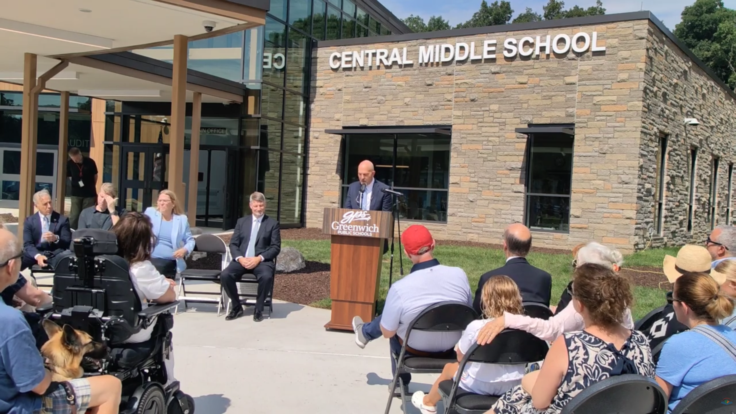 Man stands at podium in front of a large crowd for opening of local middle school.