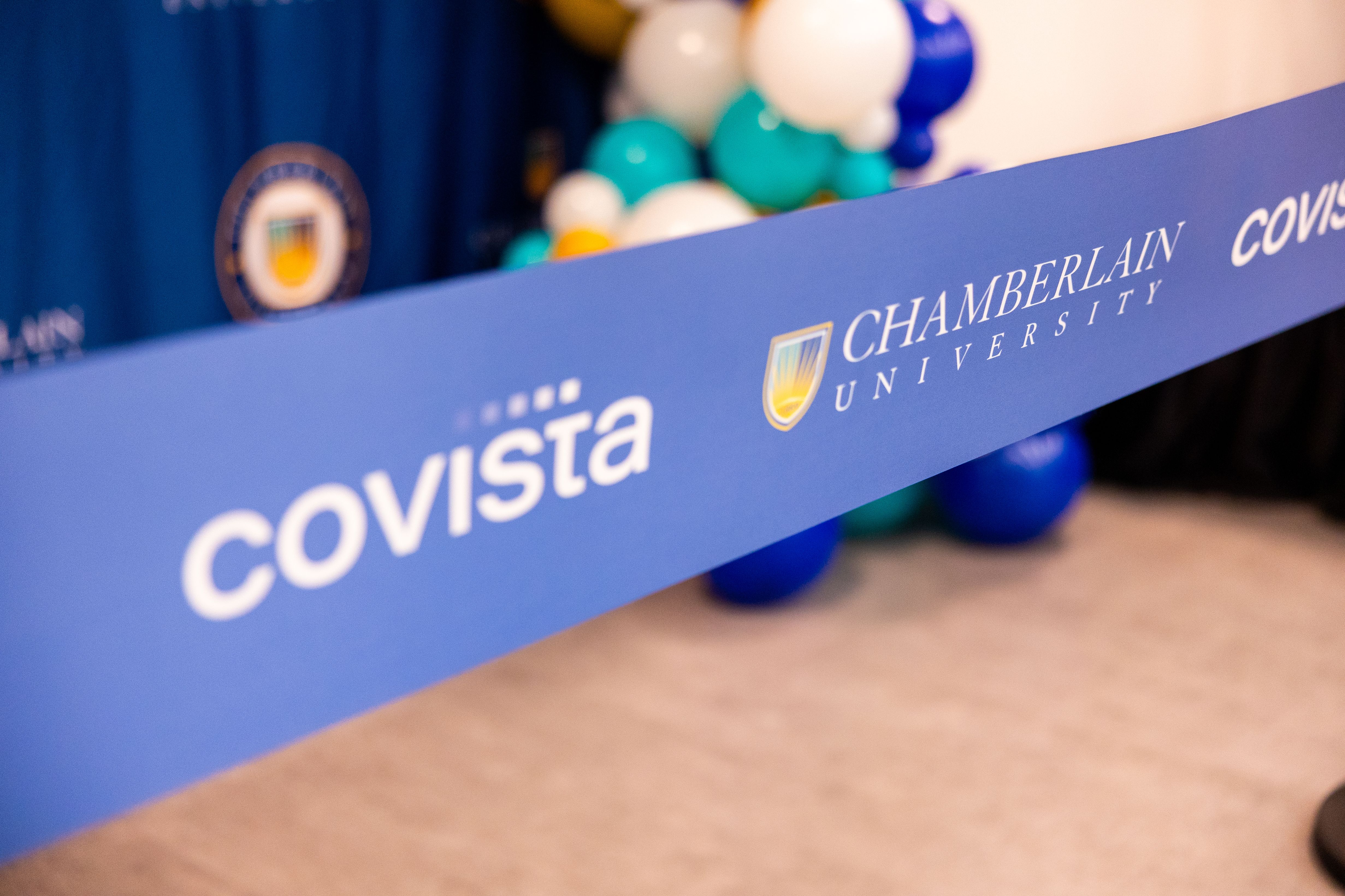 Blue ribbon for cutting that says Covista and Chamberlain University at ceremony.
