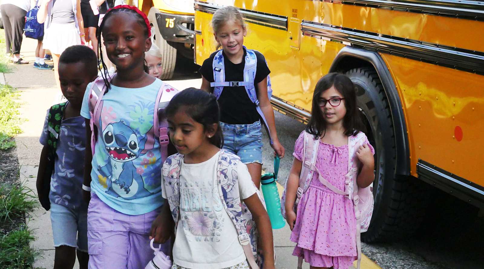 Students wearing backpacks walk beside a yellow school bus at Chesterfield Elementary.