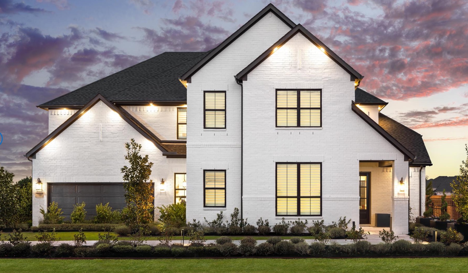 White home with black roof and windows with inside lights on.