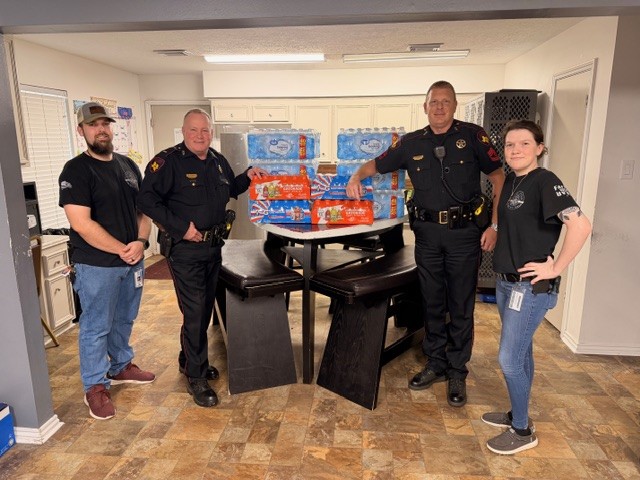 Law enforcement officers and community members gather around a table filled with donated cases of bottled water.