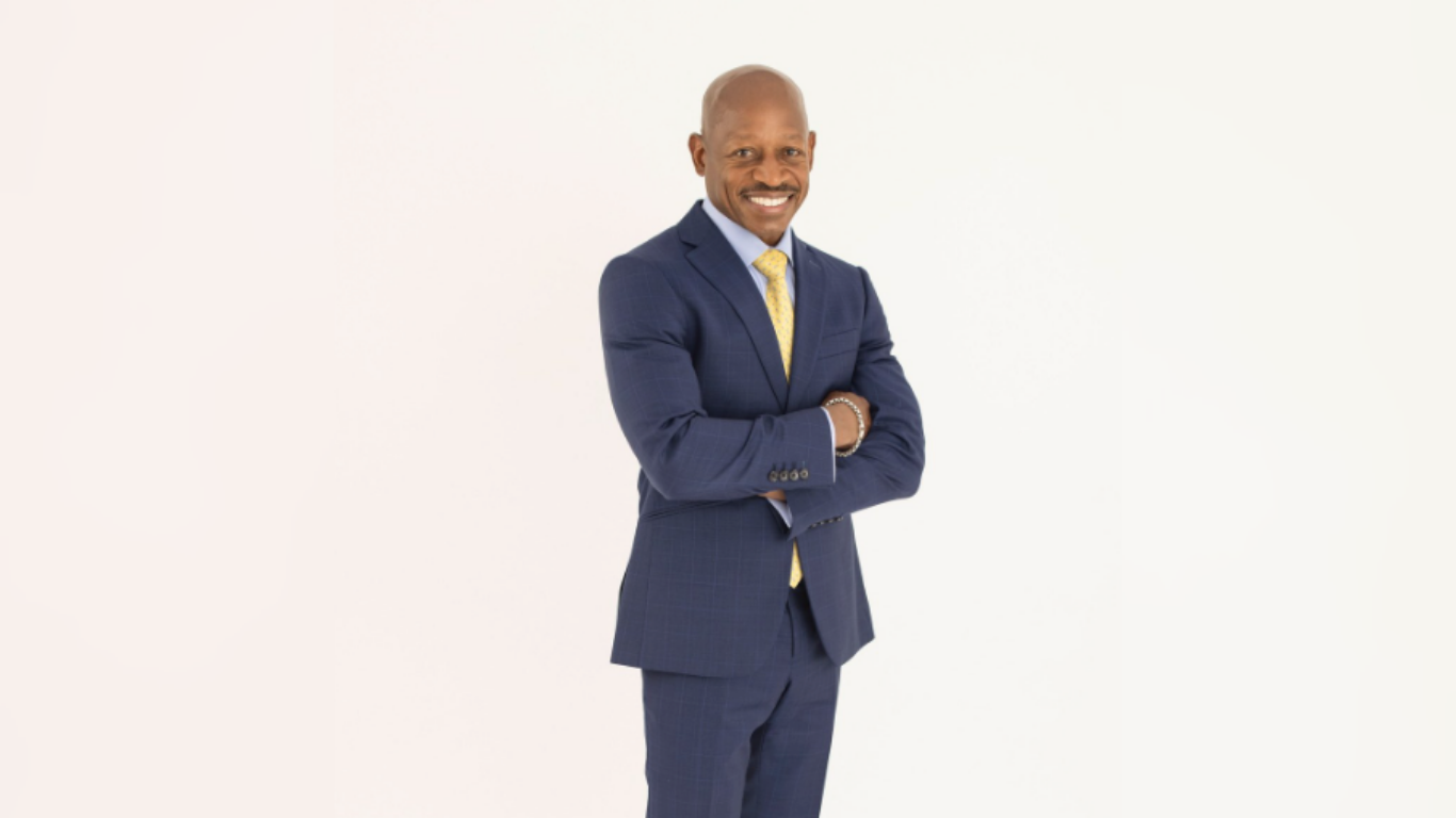 Man in suit wearing yellow tie smiling for photo with arms crossed.