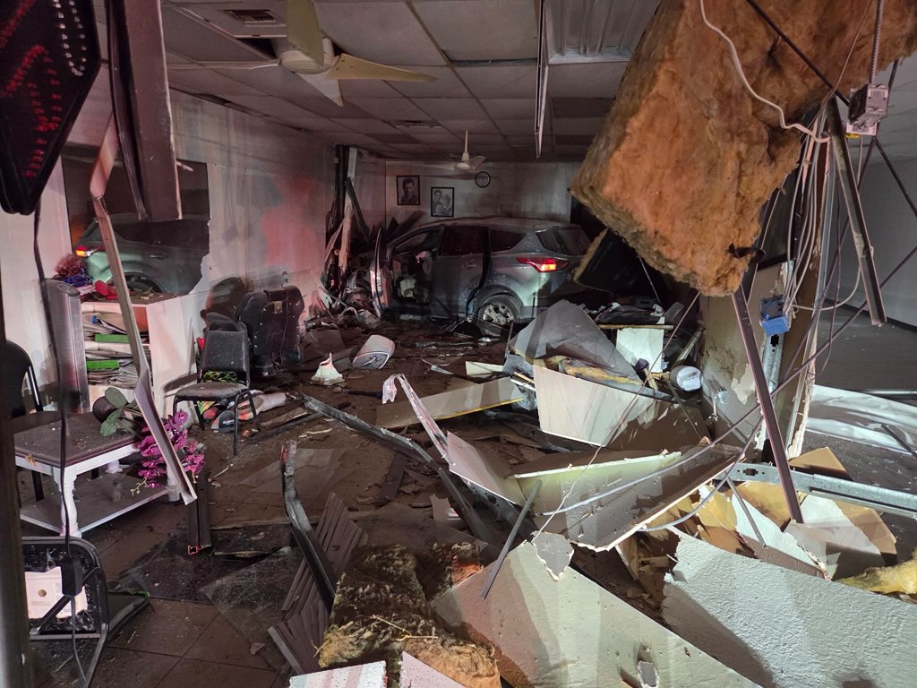 Silver car in the middle of room of building after crashing through.