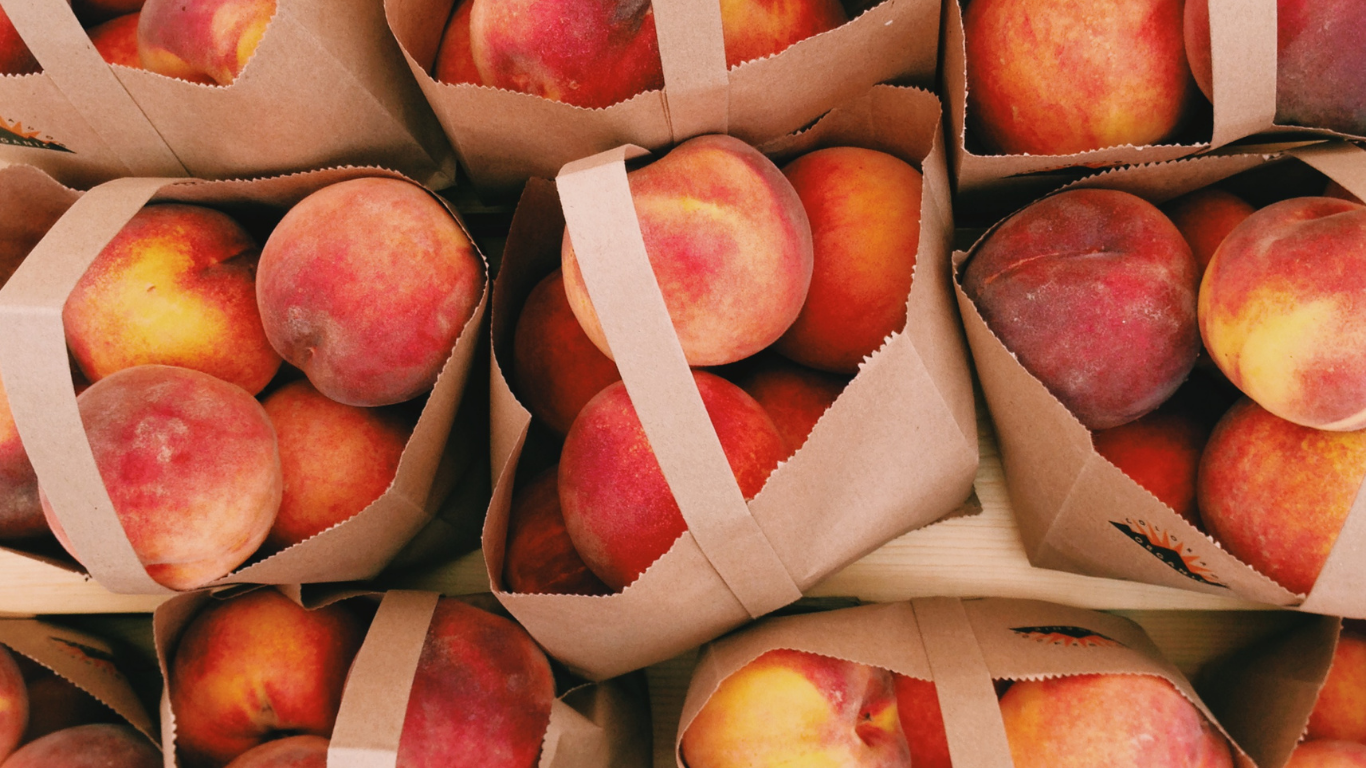 Fresh peaches displayed in paper bags at a farmers market.