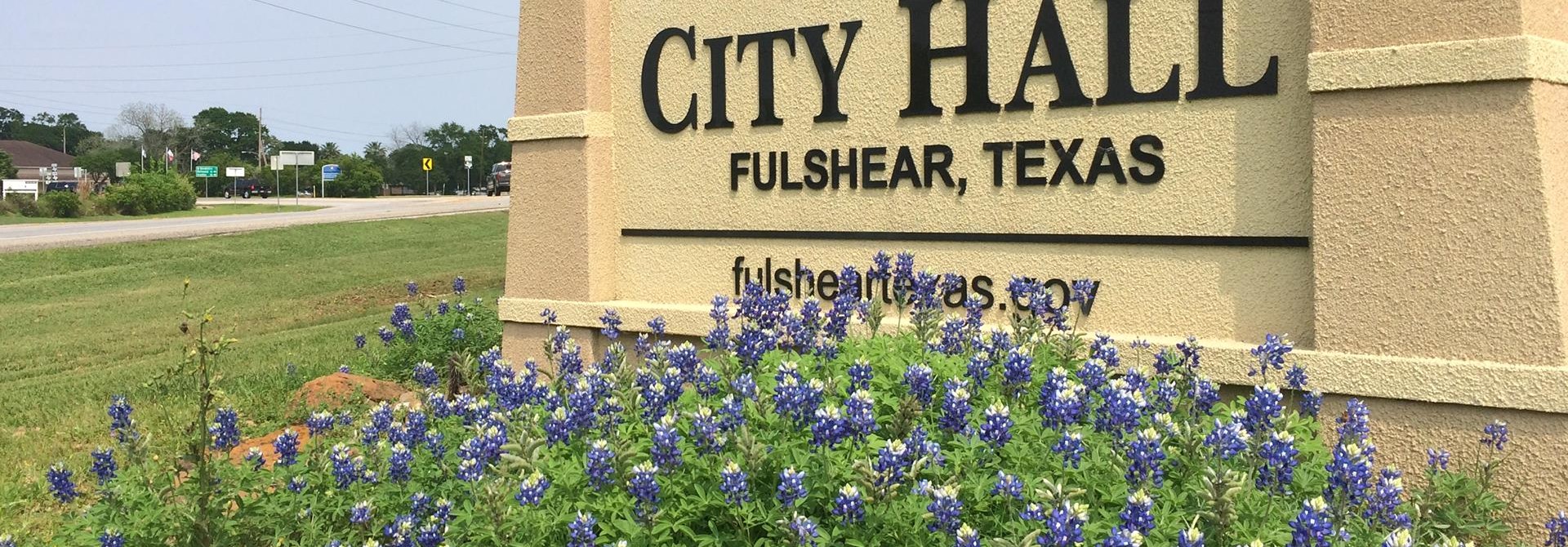 Flowers in bloom in front of city hall sign.
