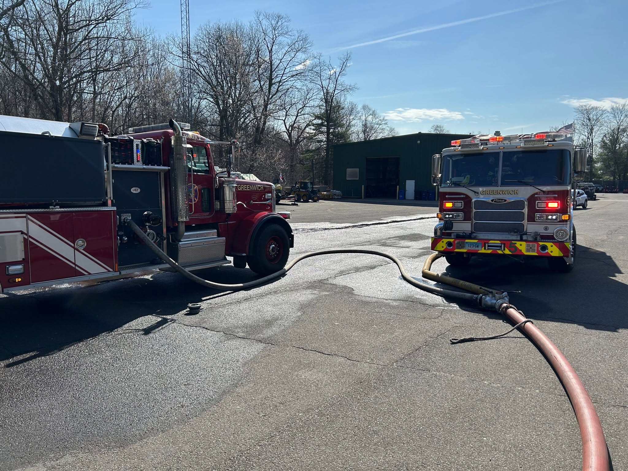 Two red fire trucks with hoses on wet pavement.